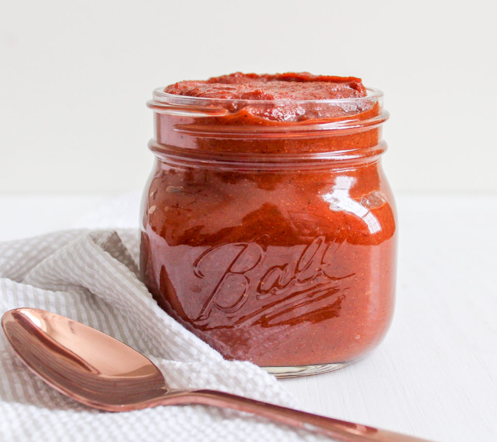 Clear glass jar filled with paleo BBQ sauce with a brass spoon in front of it 