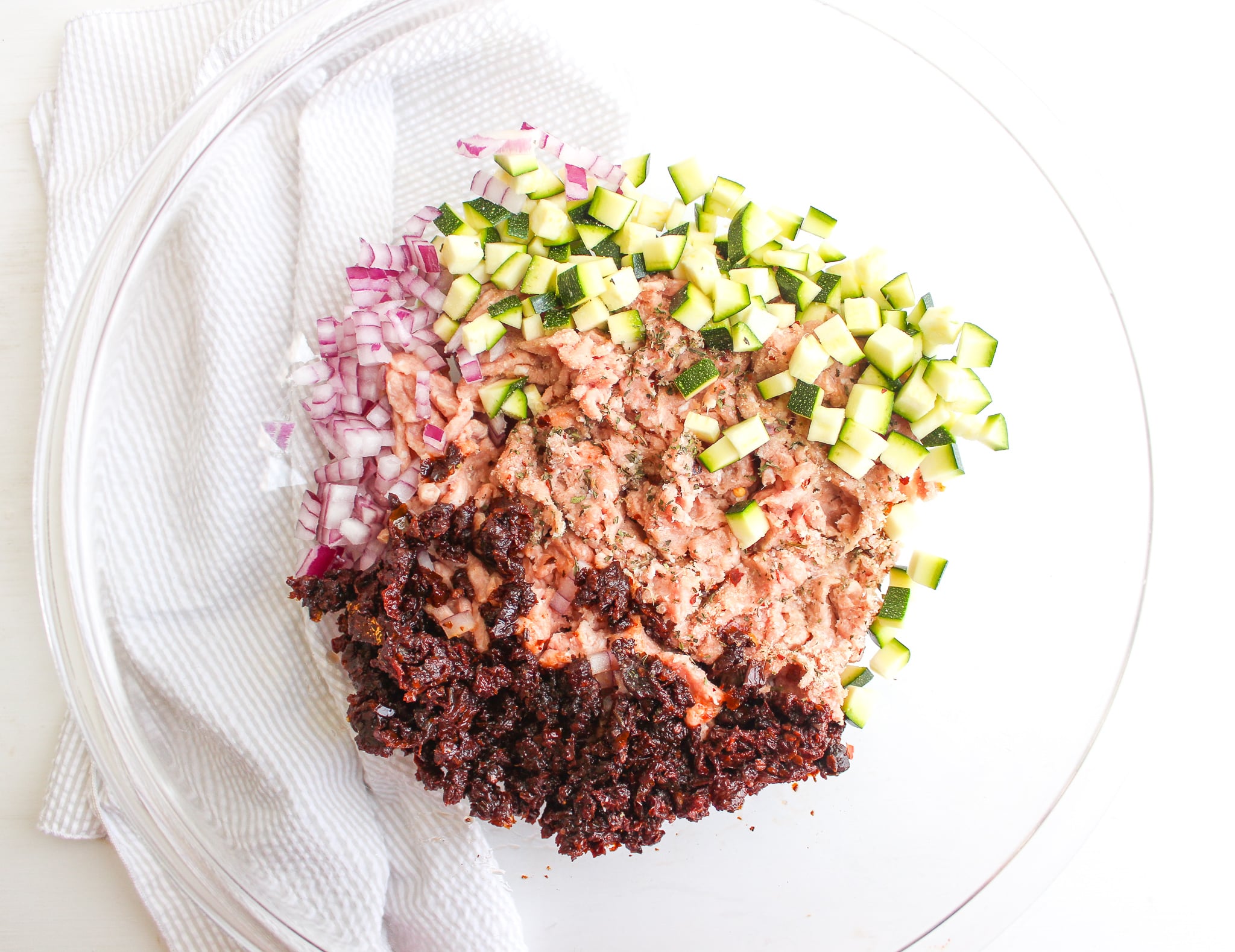 Bowl of ground turkey, diced red onion, diced zucchini, and chopped sun-dried tomatoes