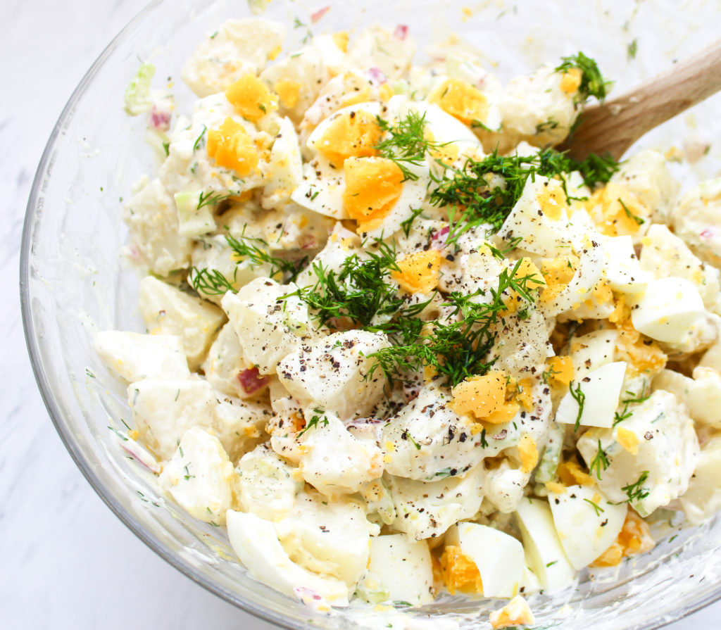 Bowl filled with potato salad and a wooden spoon leaning against it. 