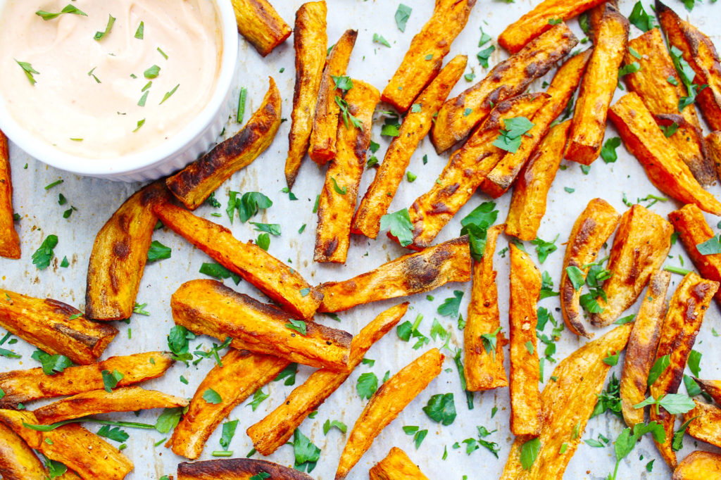 Crispy Sweet Potato Fries on a sheet pan, topped with fresh parsley and a side of aioli 