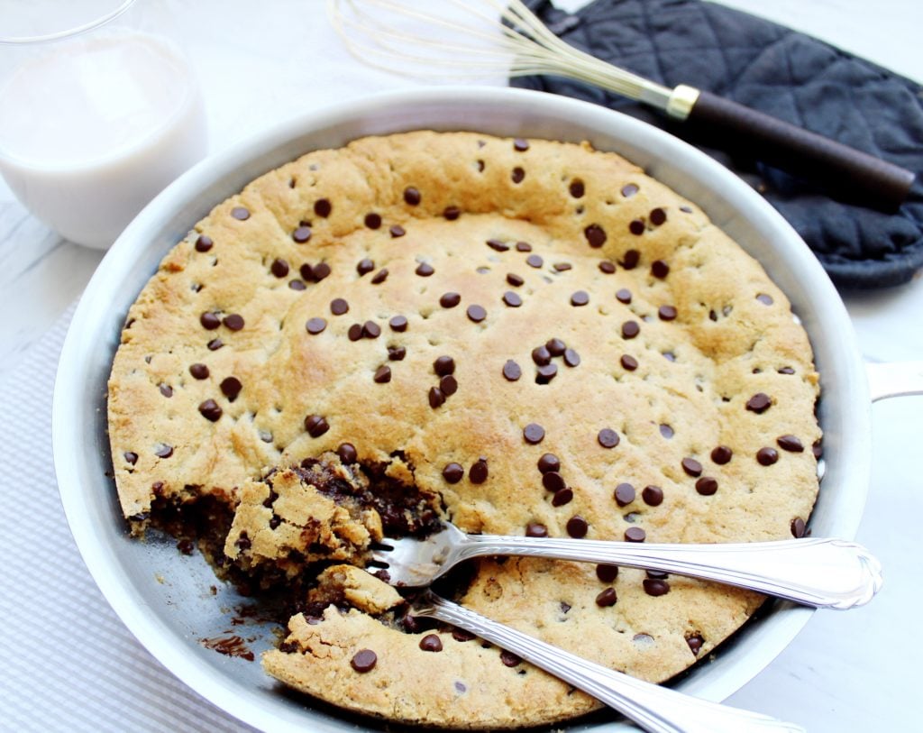 Paleo Chocolate Chip Cookie Skillet paleo chocolate chip cookie skillet with two forks in it, a glass of milk on the side, and a whisk