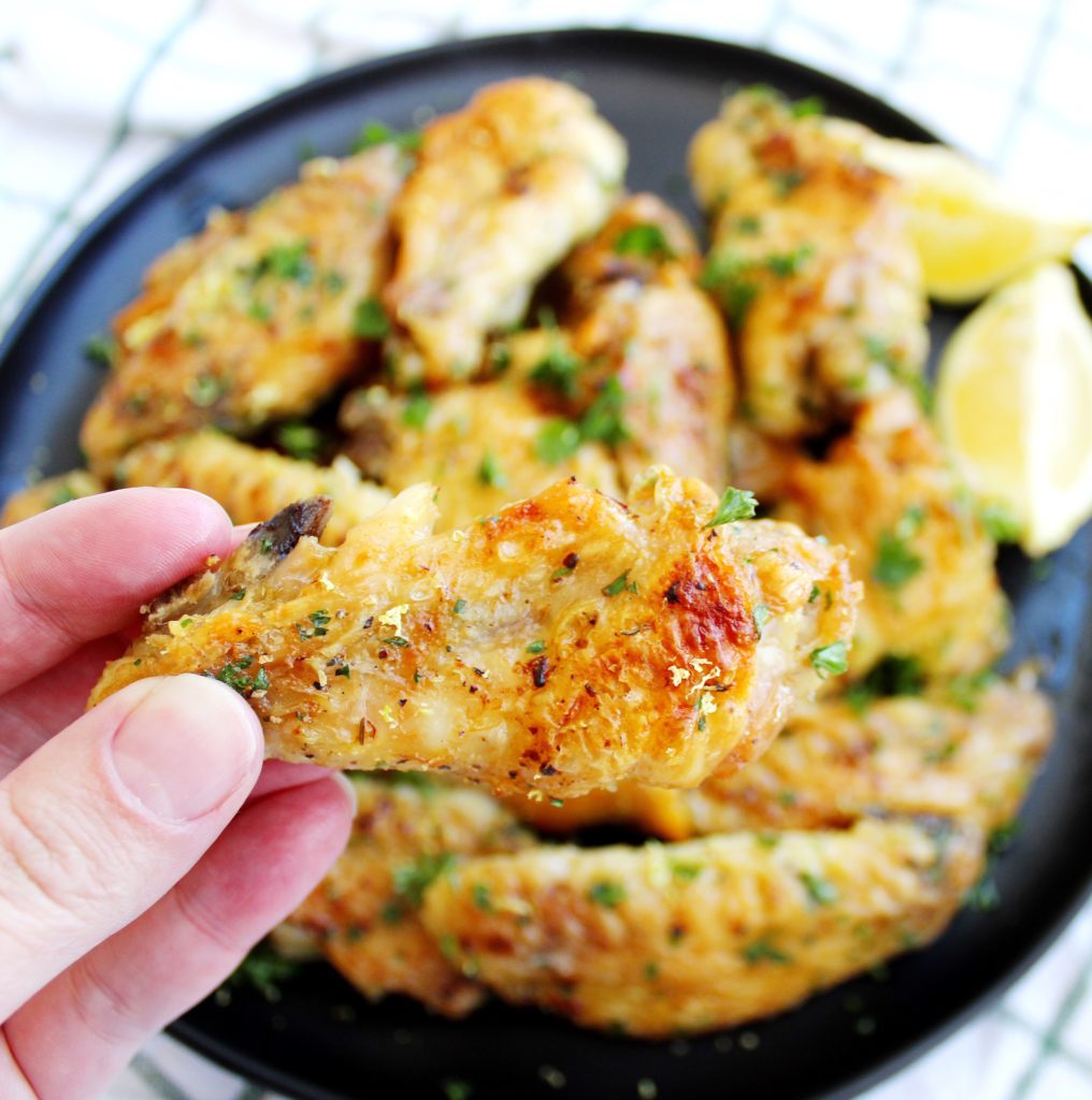 Hand holding a crispy lemon pepper chicken wing topped with fresh parsley and lemon zest 