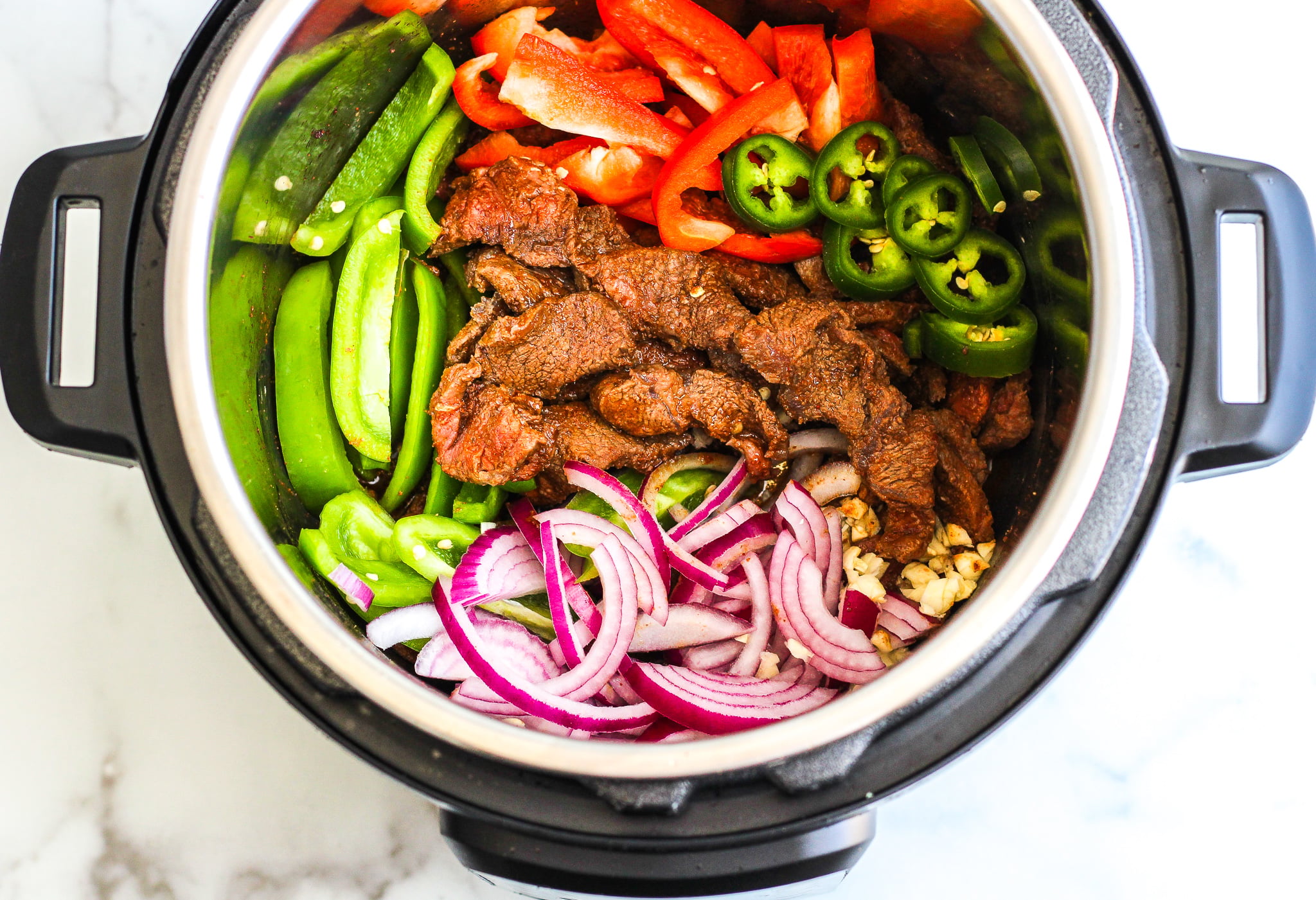 Instant Pot filled with sliced steak, red onions, jalapeños, sliced bell peppers, and minced garlic 
