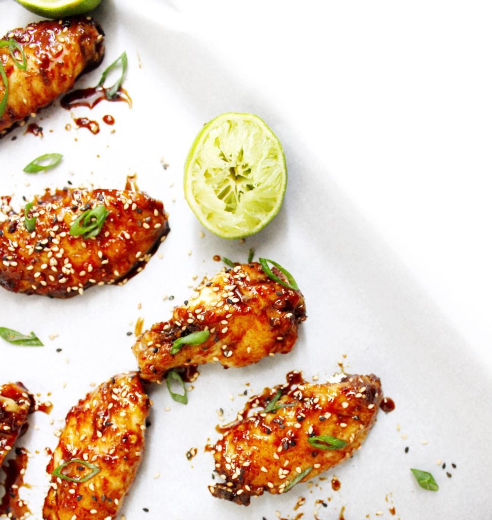 Chicken wings coated in a sweet and spicy asian sauce and topped with sesame seeds and fresh cilantro with squeezed limes on the side 