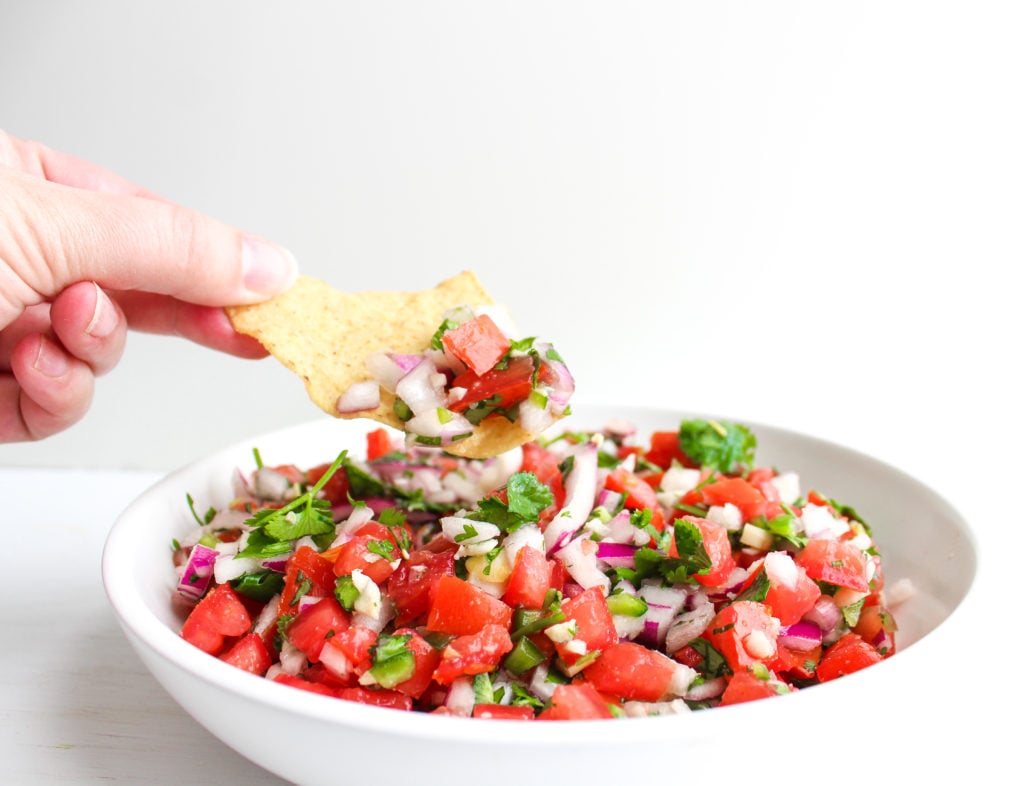 Hand holding tortilla chip dipped in pico de Gallo 