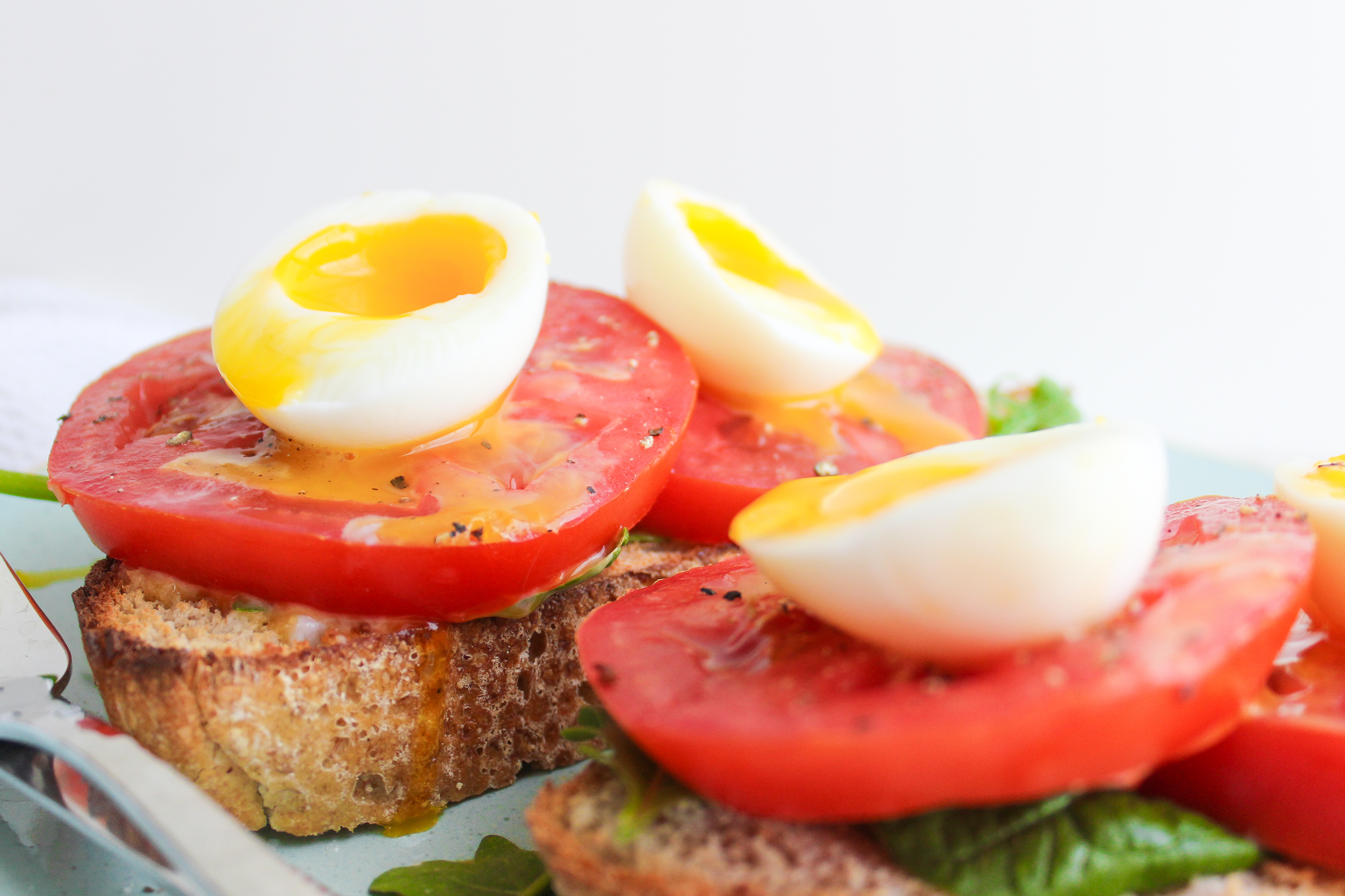 Sourdough toast topped with fresh greens, tomato slices and jammy eggs with the yolks running down