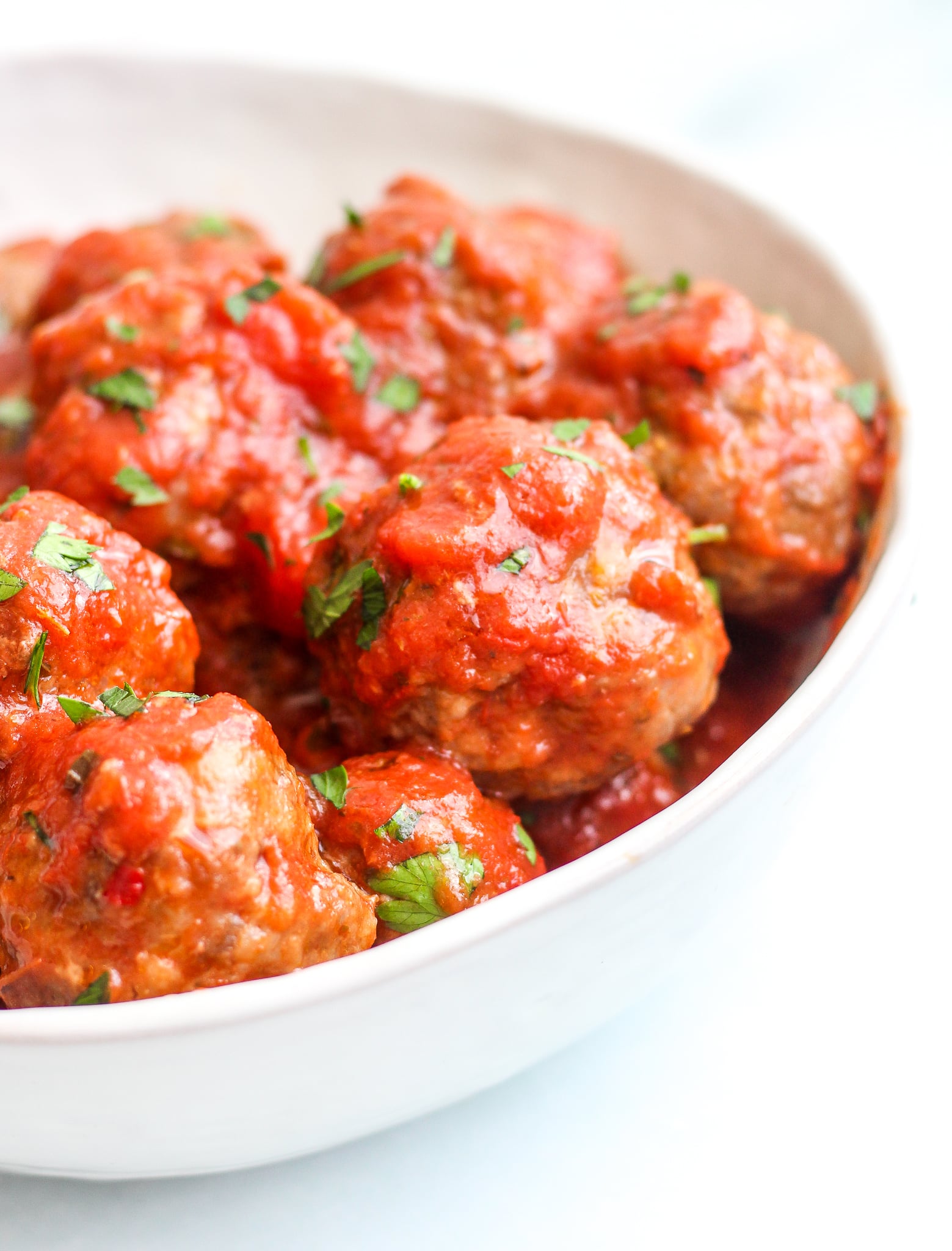 Baked Italian meatballs in a red sauce topped with fresh parsley and served in a white bowl 