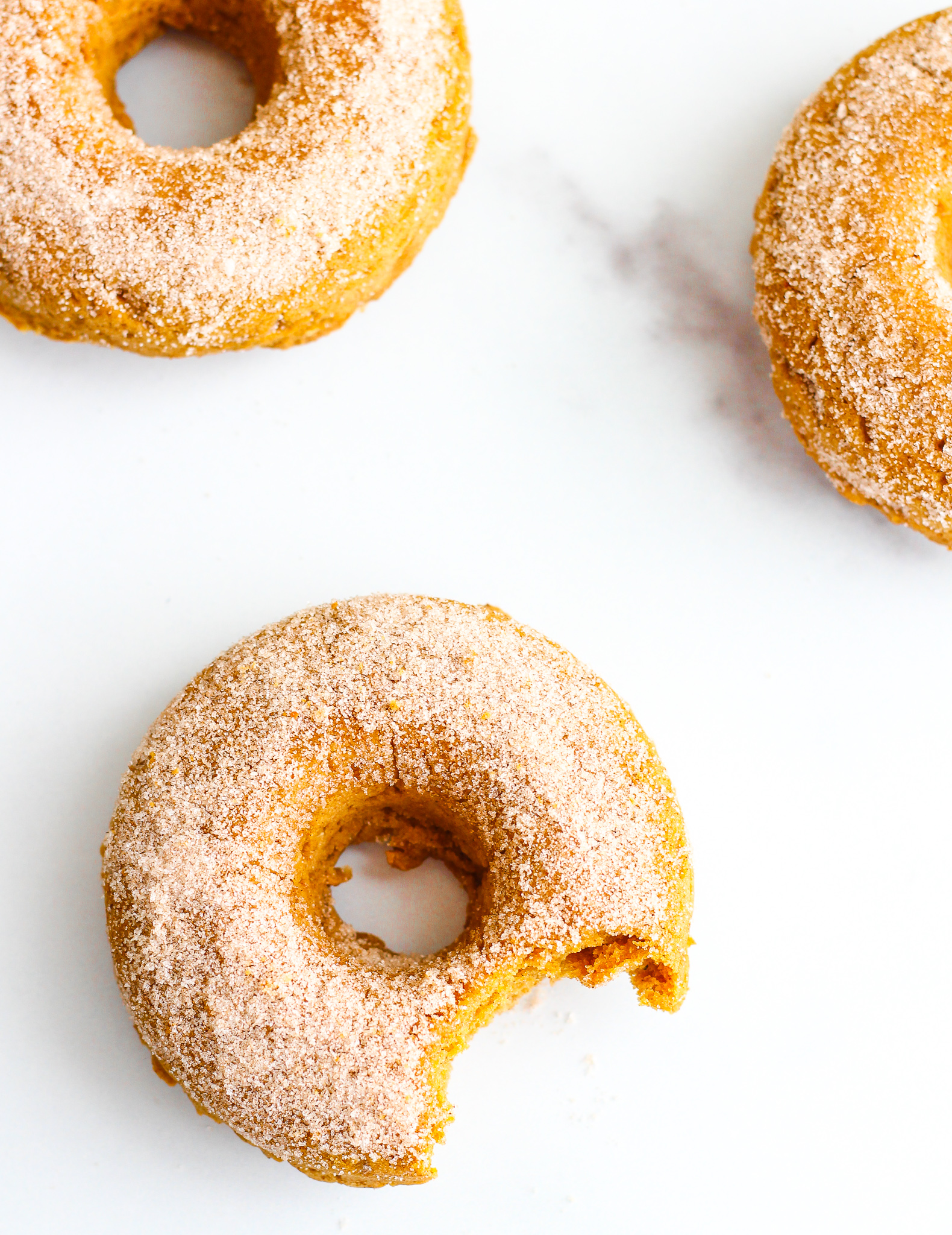 Gluten Free Pumpkin Spiced Donuts laying on a white marble surface 