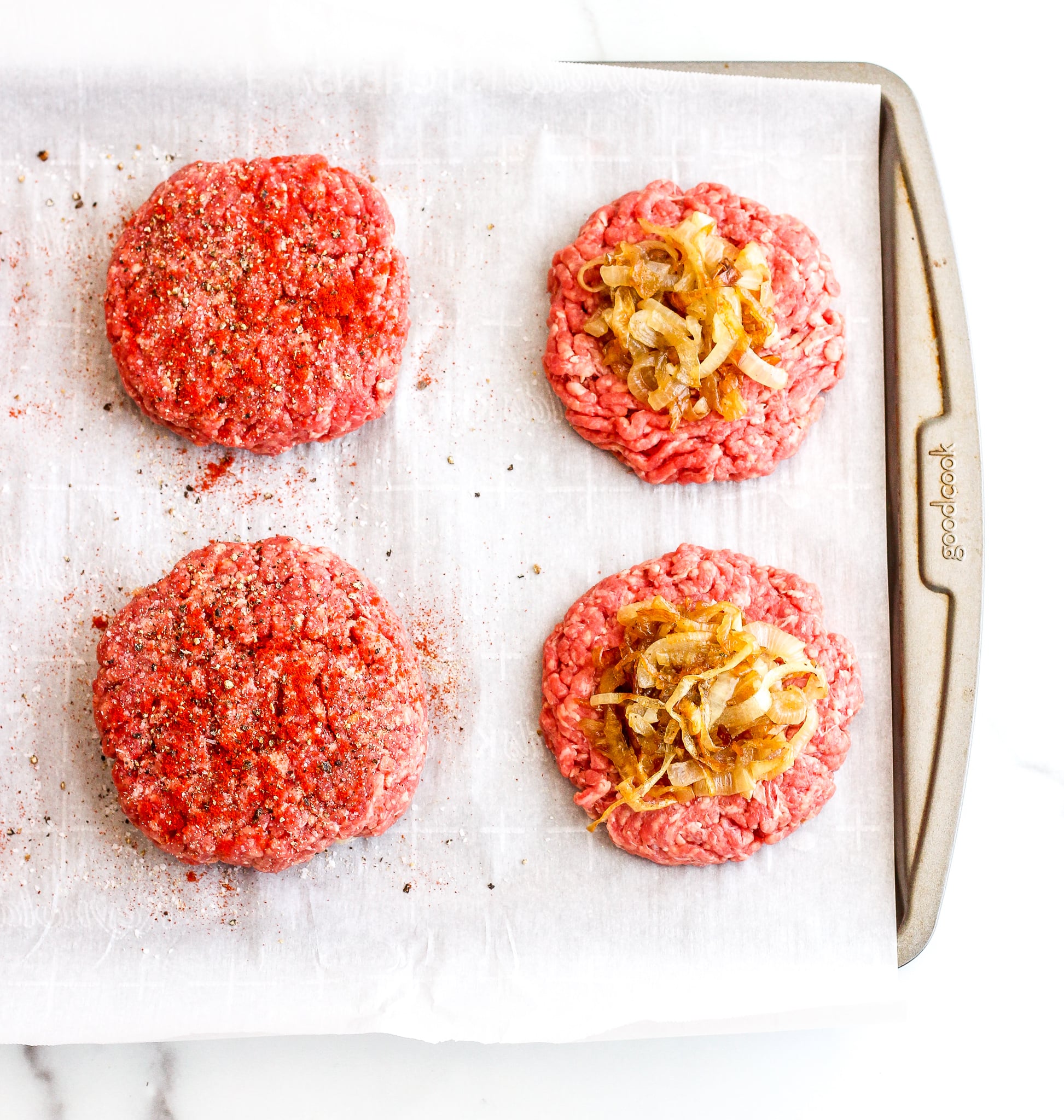 Caramelized Onion Stuffed Burgers Raw burger patties on a lined baking sheet being stuffed with caramelized onions