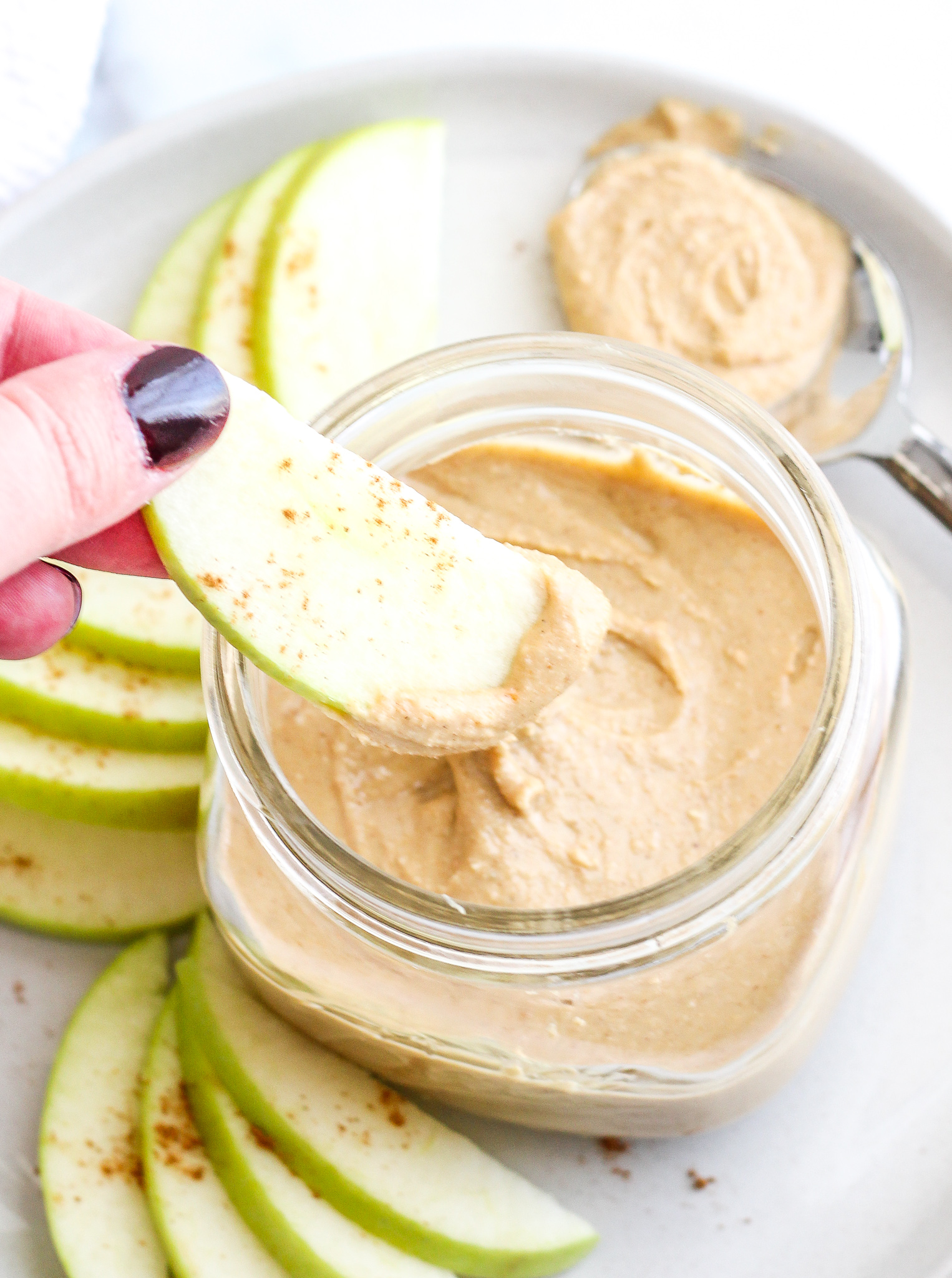 Hand dipping green apple slice into pumpkin spice cashew butter