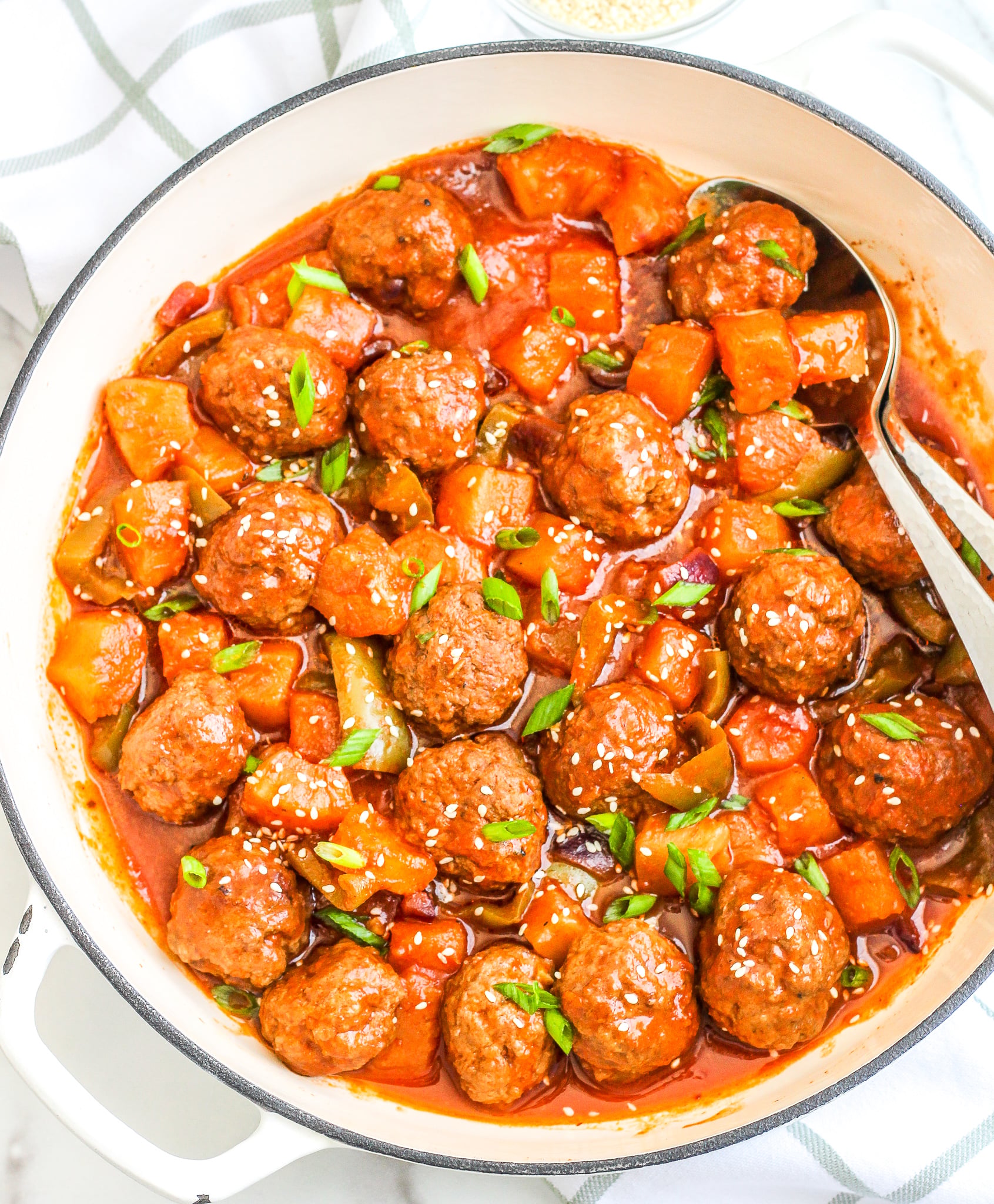 Sweet & Sour Meatballs in a large white skillet topped with sliced green onions