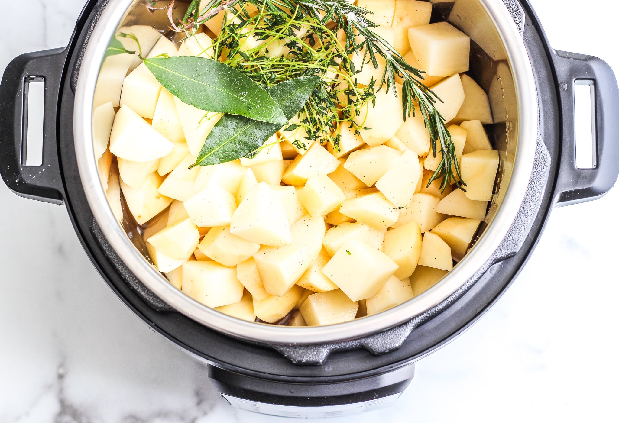 Cubed potatoes in an instant pot with fresh herbs and salt 