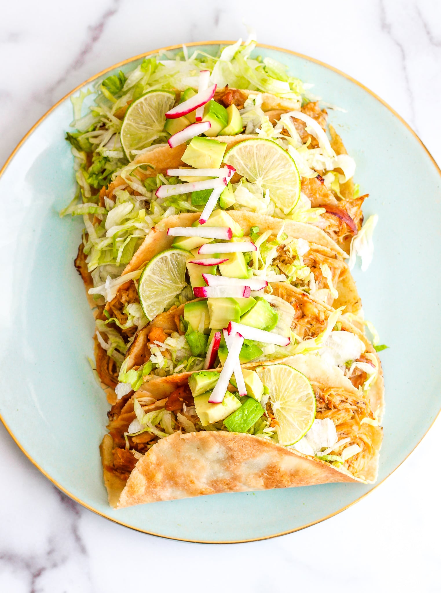 Overhead shot of baked chicken tacos loaded up with avocado, limes, radishes and shredded lettuce