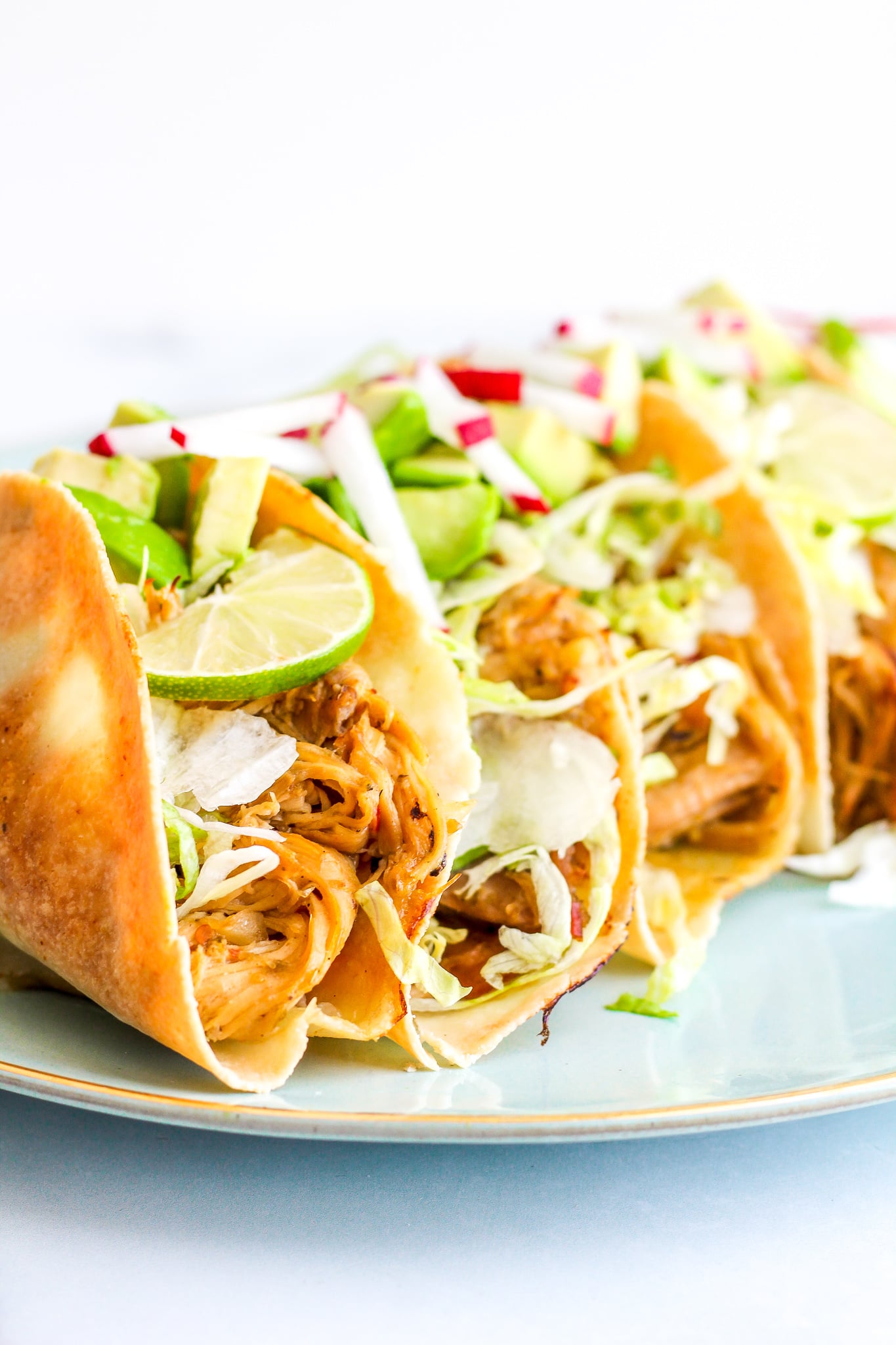 Side view of staked baked chicken tacos topped with lime slices, diced avocado and radish