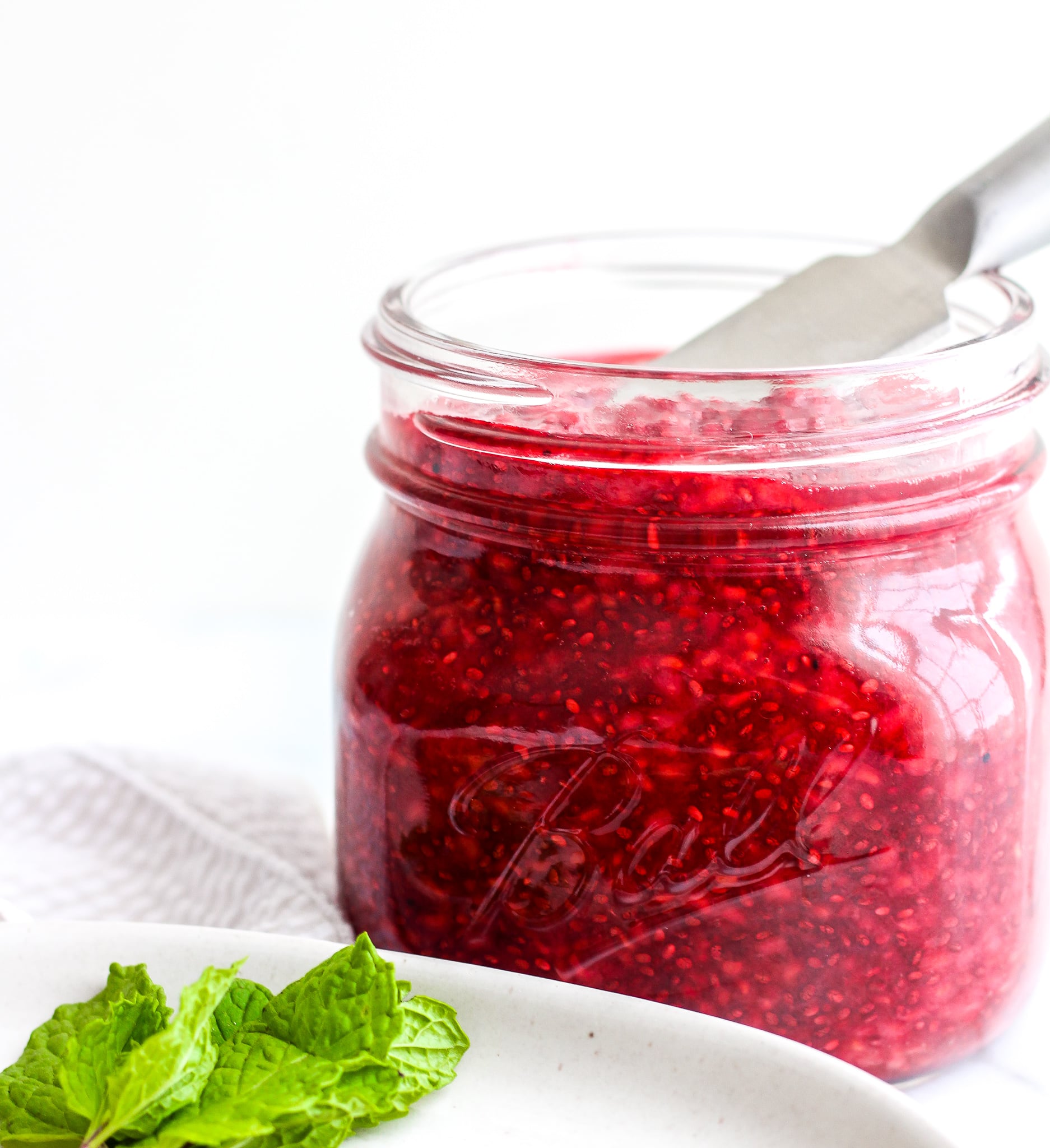 Easy Raspberry Chia Seed Jam in a glass jar with a serving utensil in it 