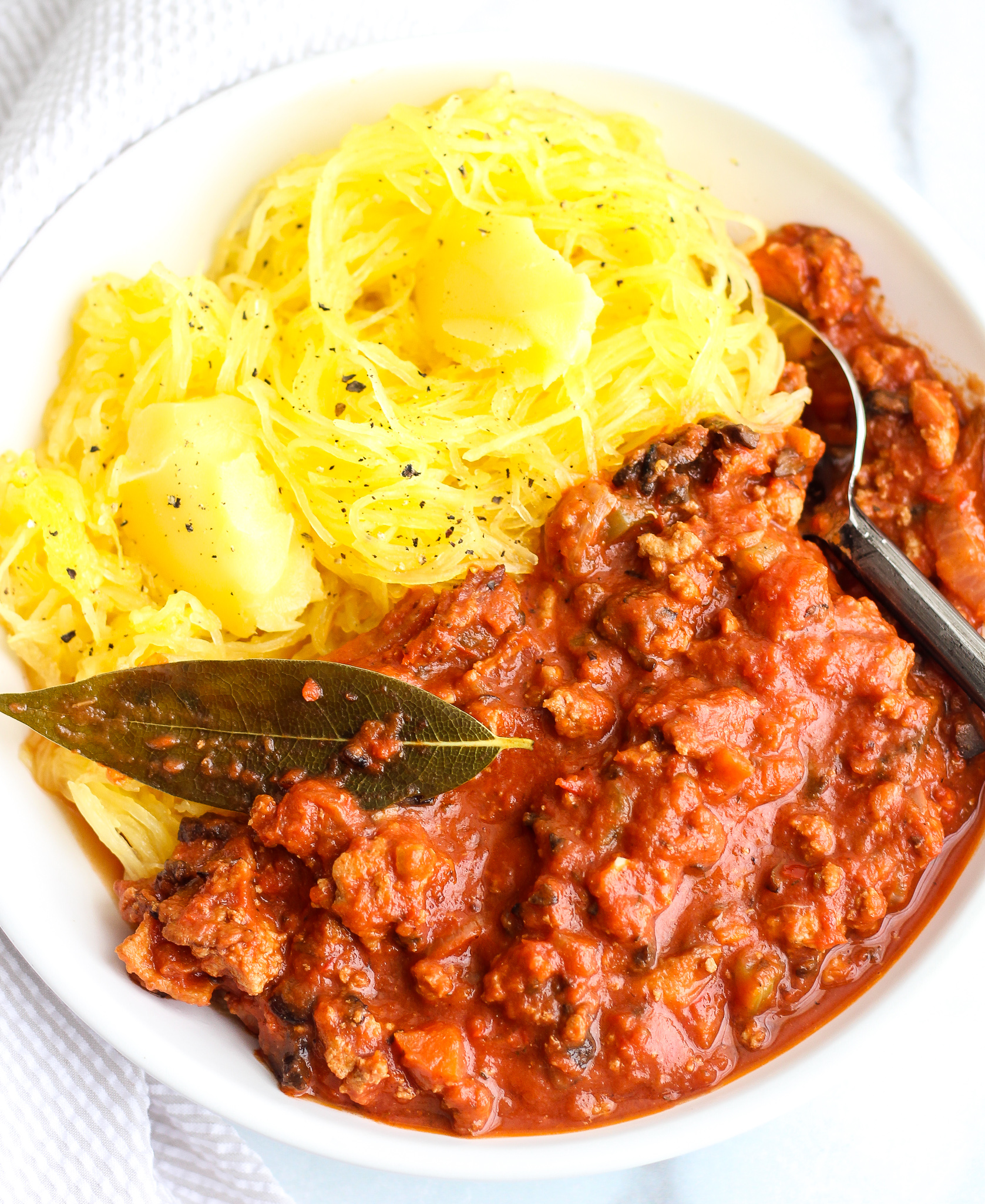 Whole30 Turkey Bolognese in a white bowl with swirled spaghetti squash topped with ghee 