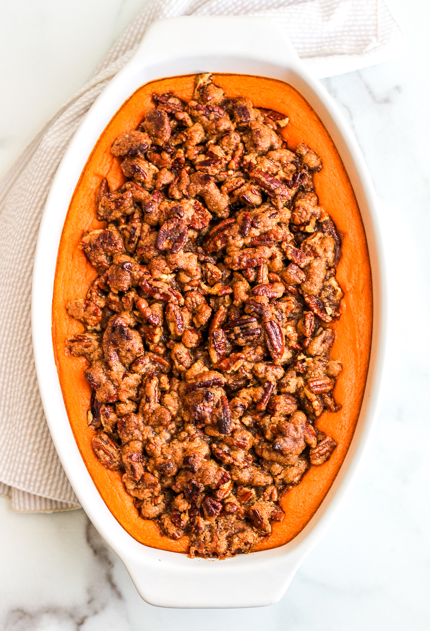 Sweet Potato Casserole topped with Pecan topping in a white serving dish 