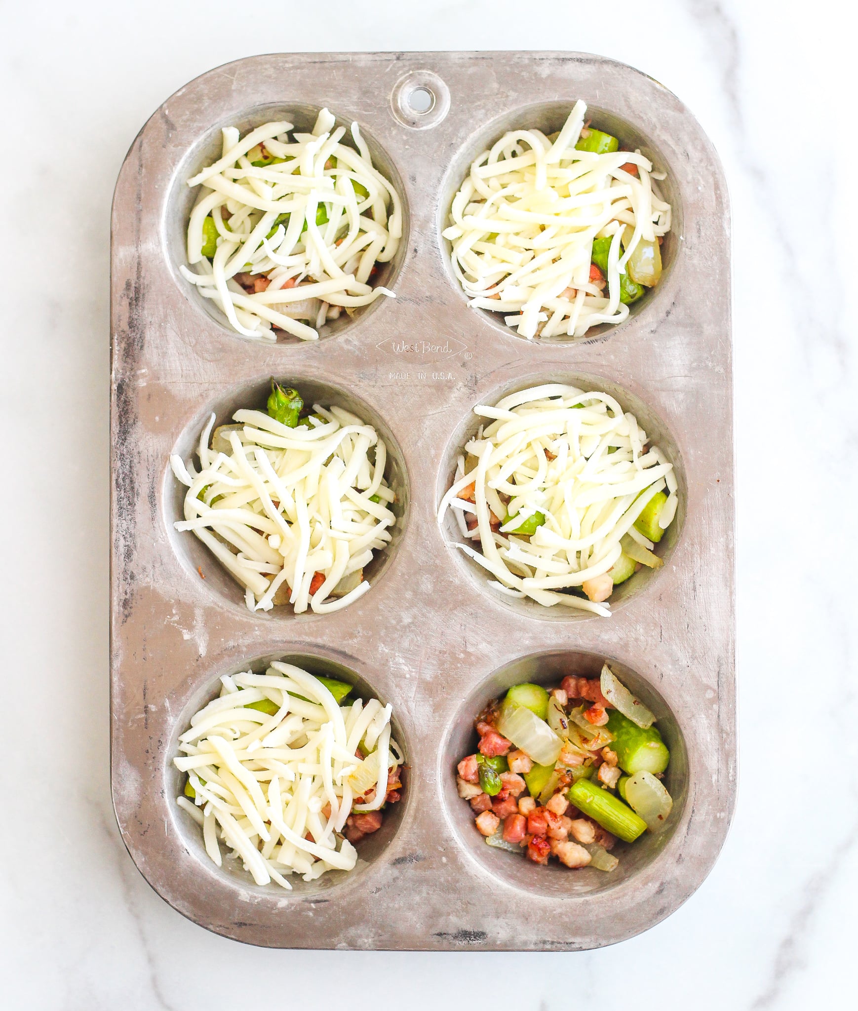 silver muffin tin filled with pancetta and asparagus topped with shredded cheese