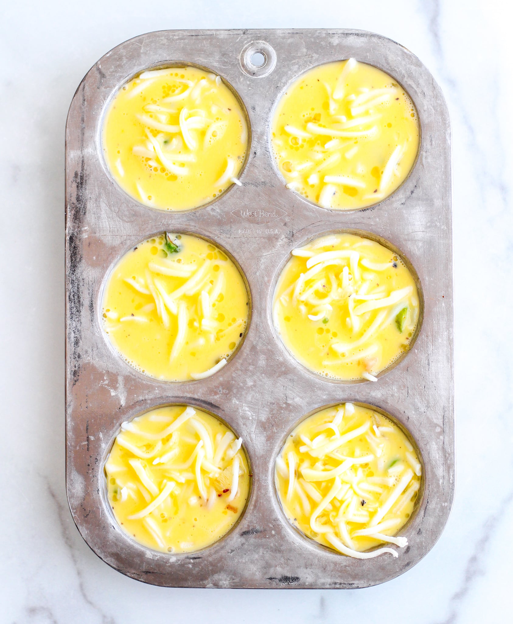 silver muffin tin filled with egg mixture