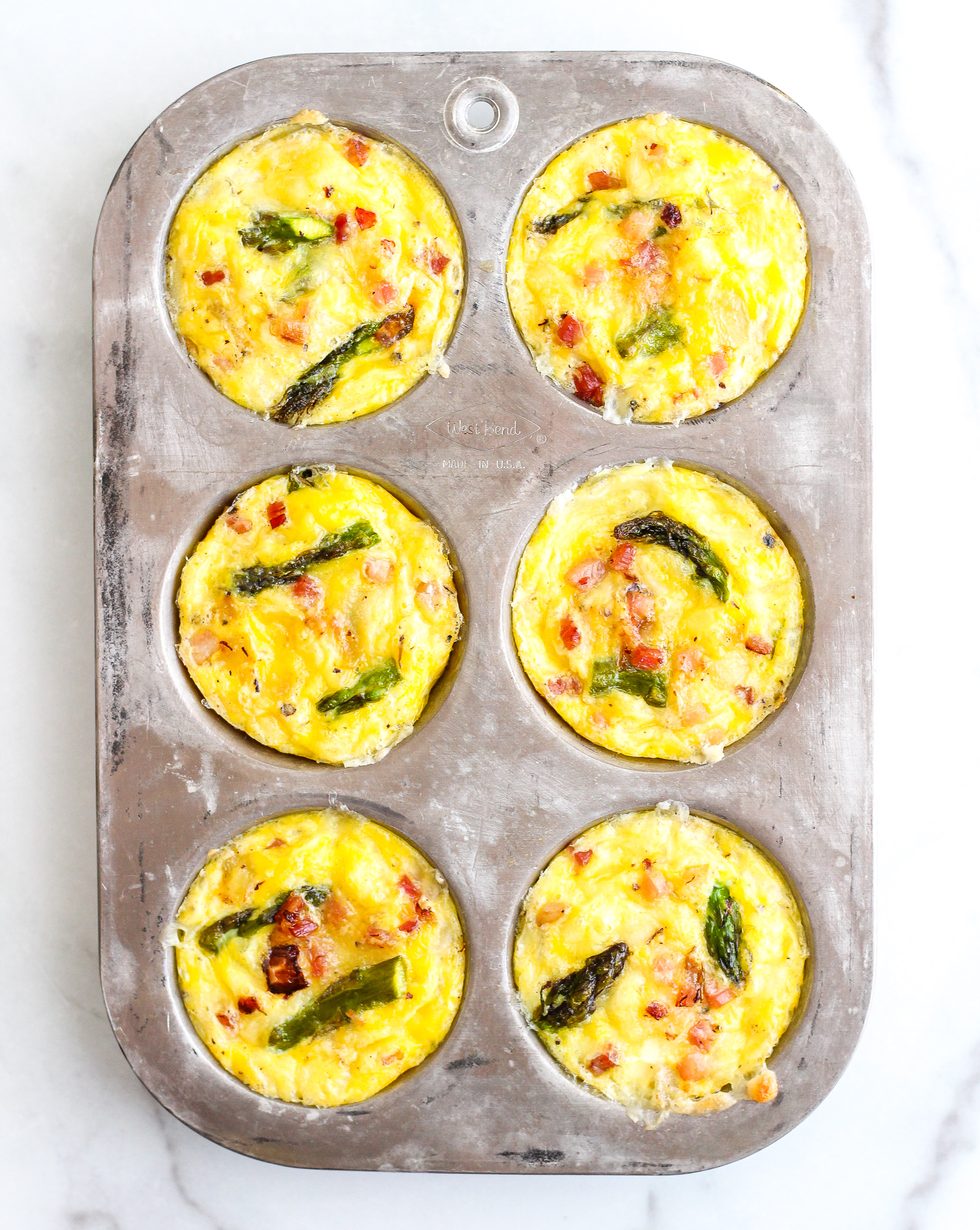 silver muffin tin with baked keto pancetta and asparagus egg muffins