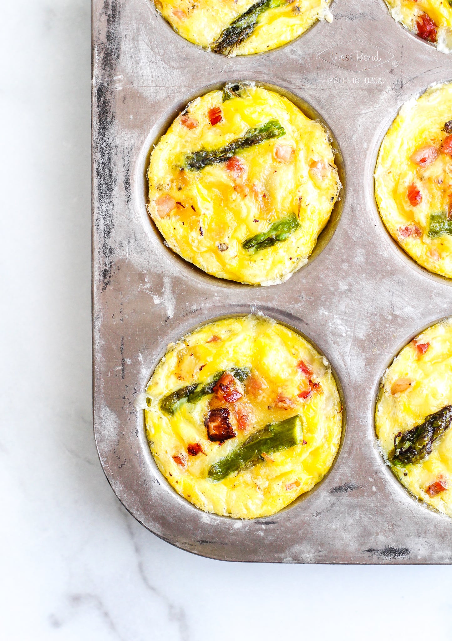 Baked keto pancetta & asparagus egg muffins in a silver muffin tin