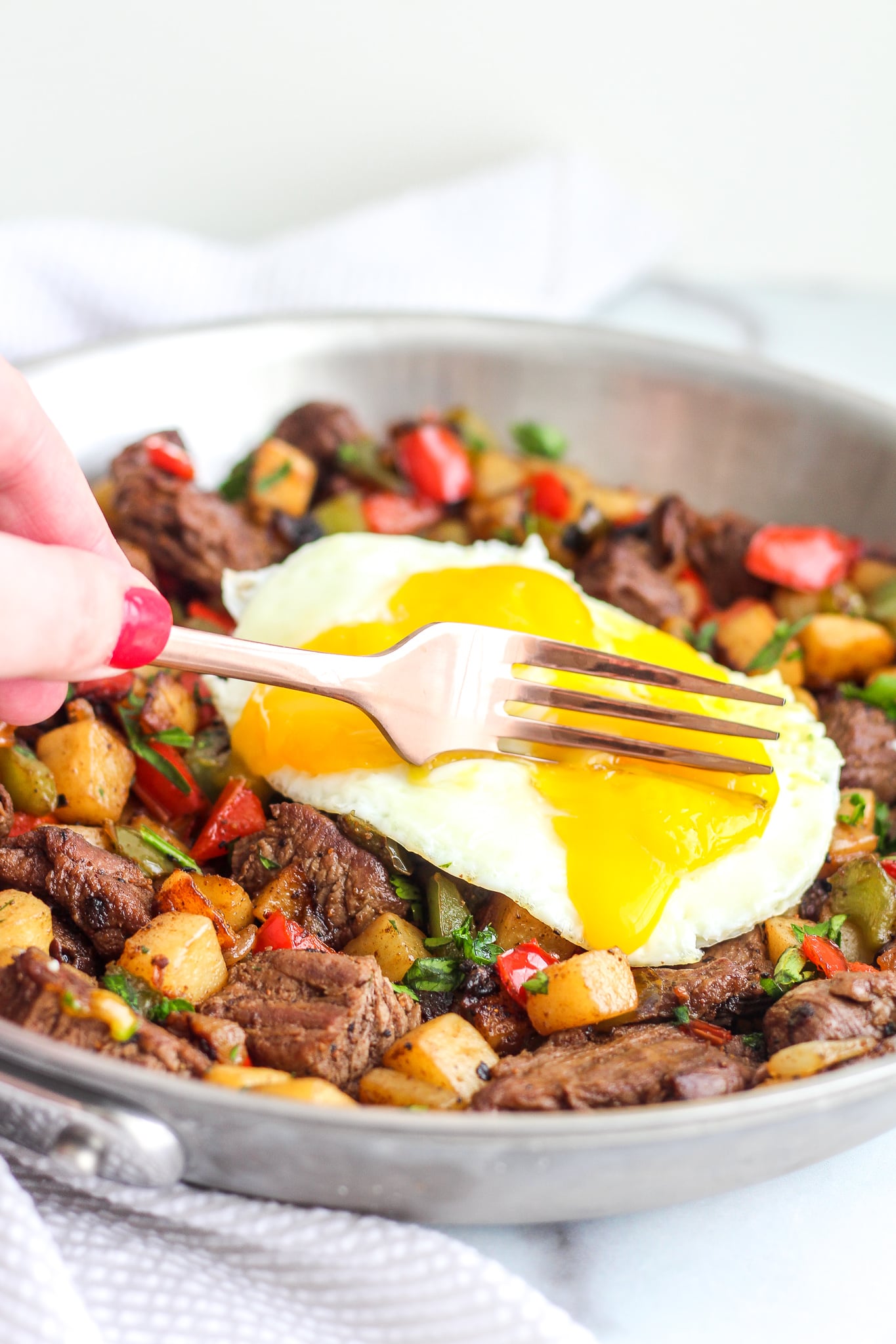Fork cutting into a perfect runny egg yolk over Whole30 Steak Breakfast Hash