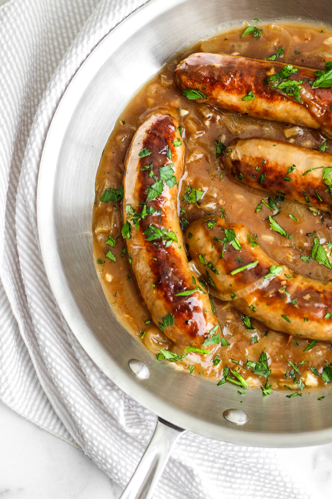 browned sausages in onion gravy in a stainless steel skillet 