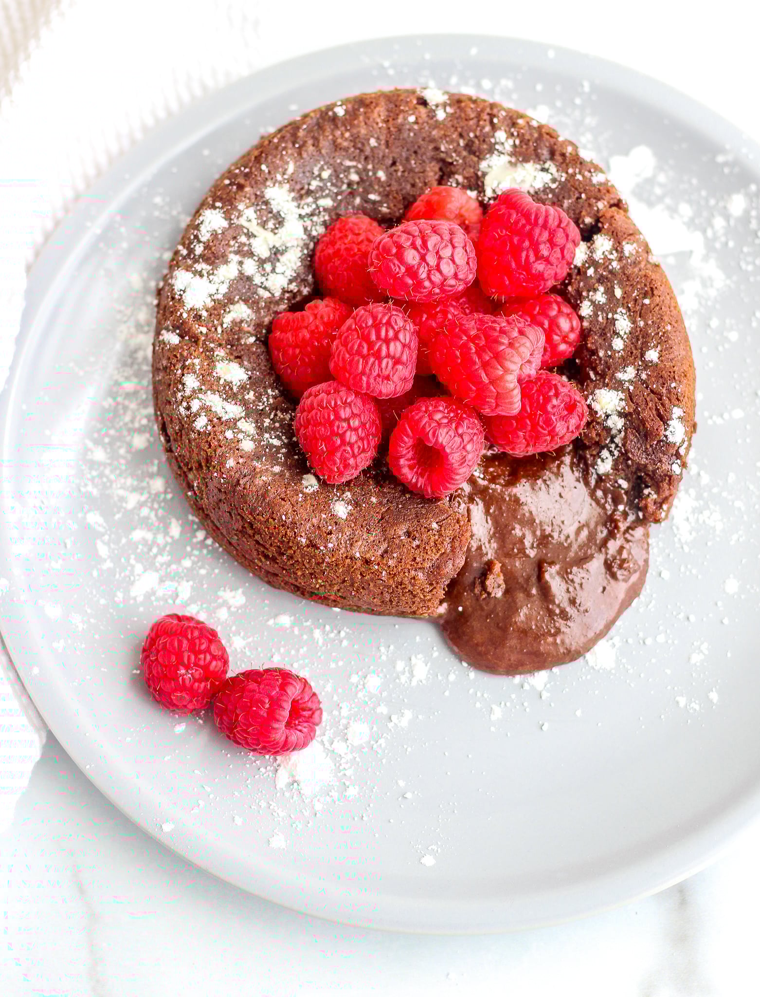 Chocolate lava cake sprinkled with confectioners sugar and topped with fresh raspberries 