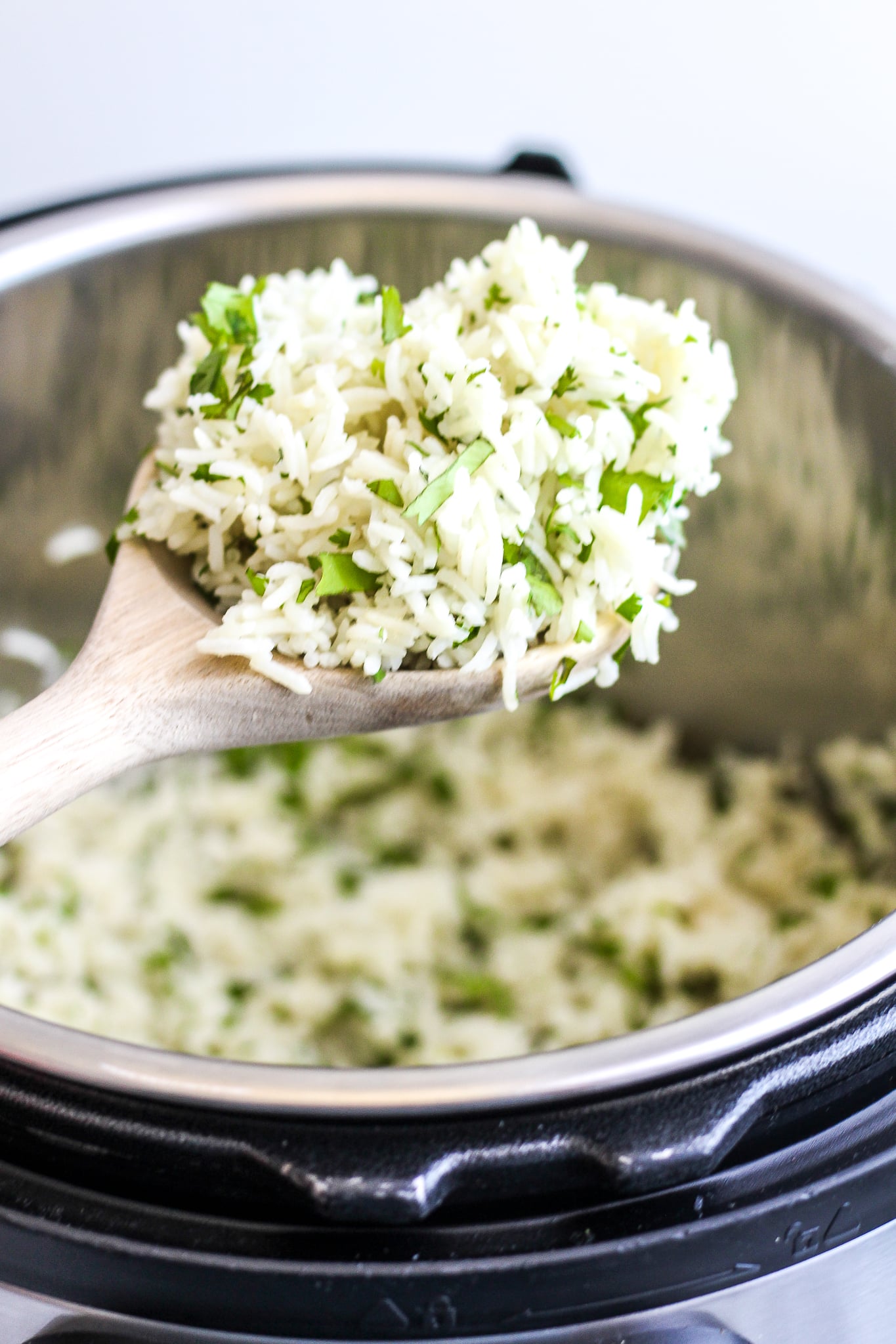 Wooden spoon holding a scoop of cilantro lime rice over the instant pot that is also filled with cilantro lime rice 