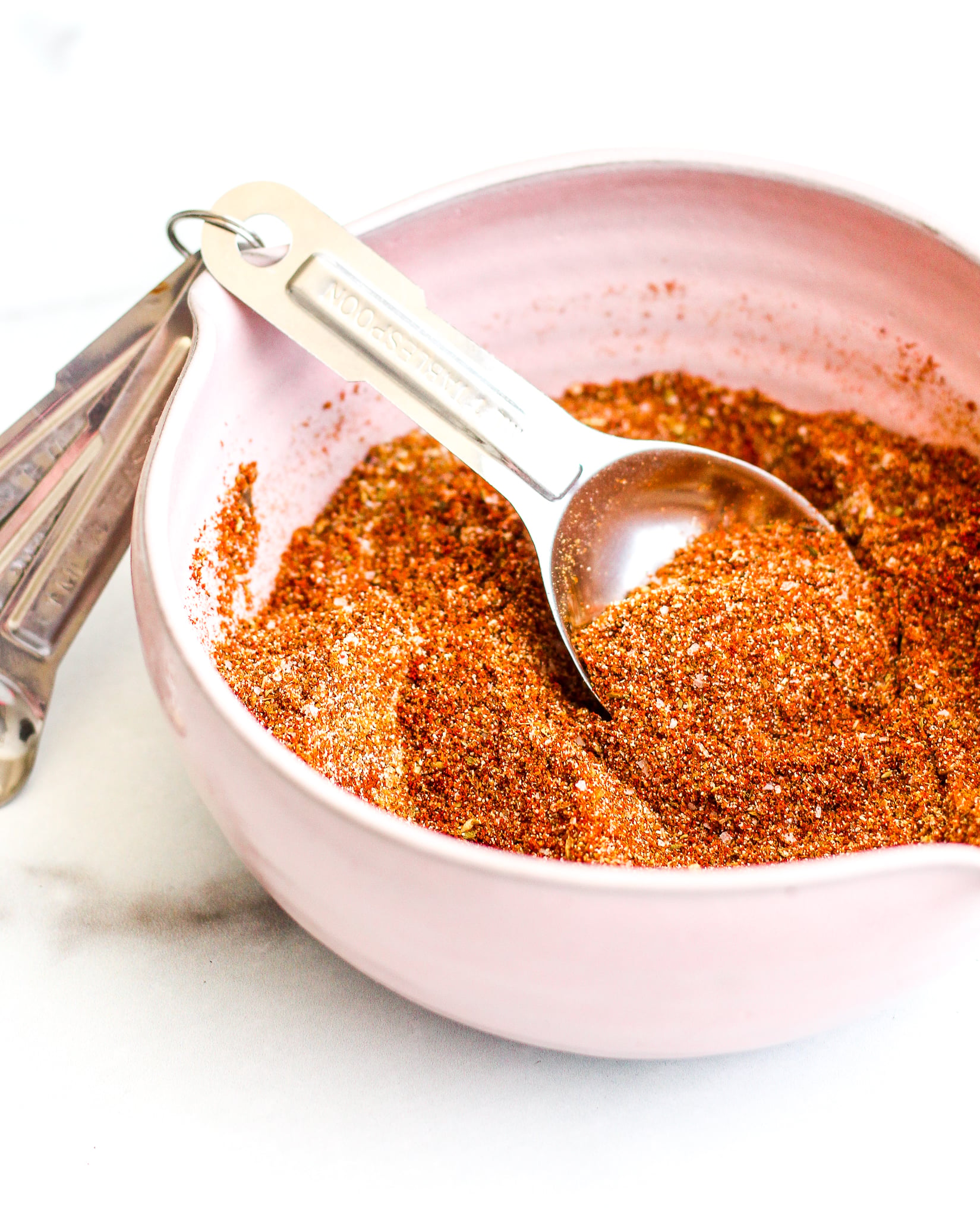 Homemade taco seasoning in a pick ceramic bowl with a silver measuring spoon inside 