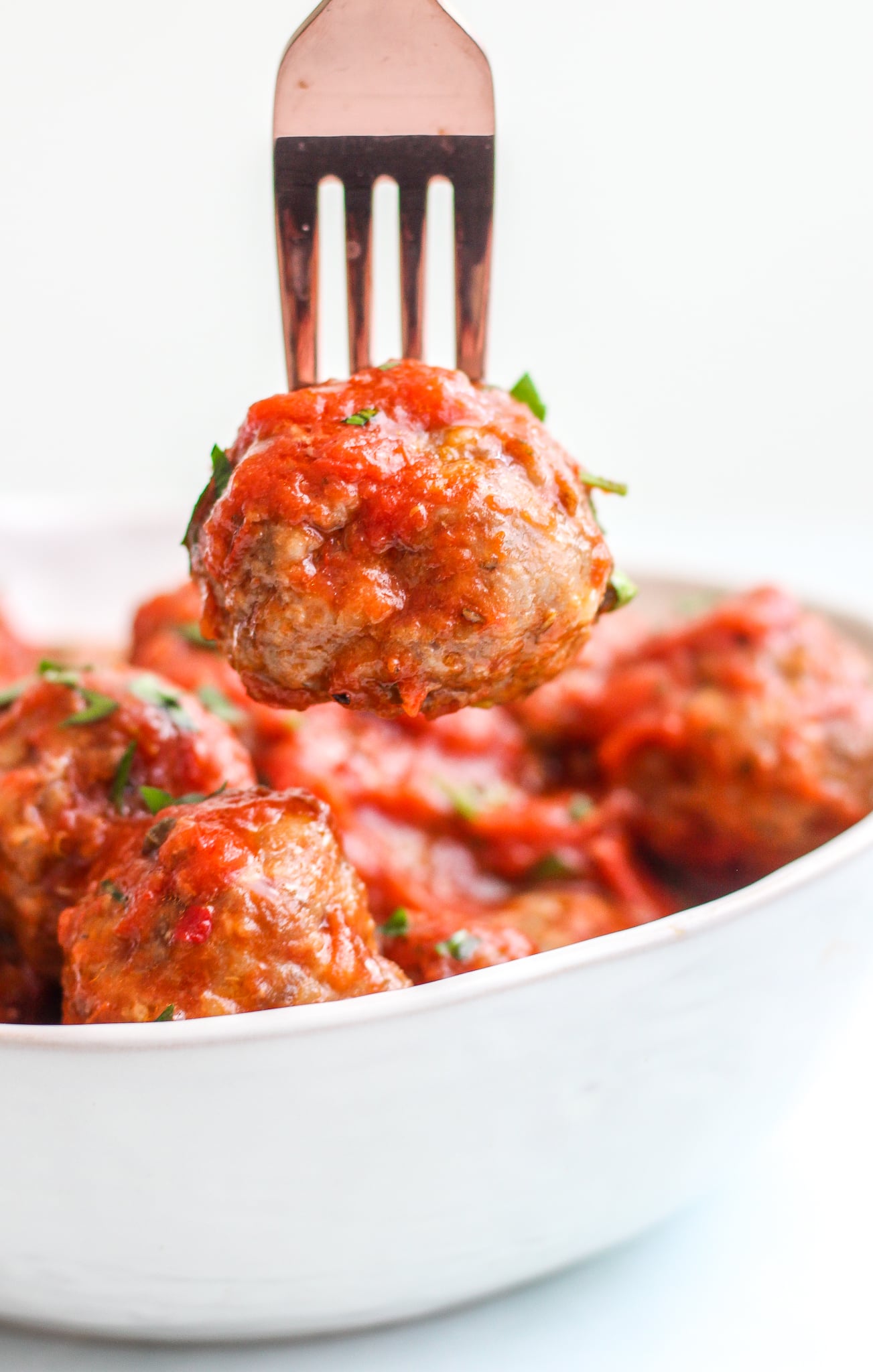 baked Italian meatball on a fork being held over a bowl of meatballs in sauce 