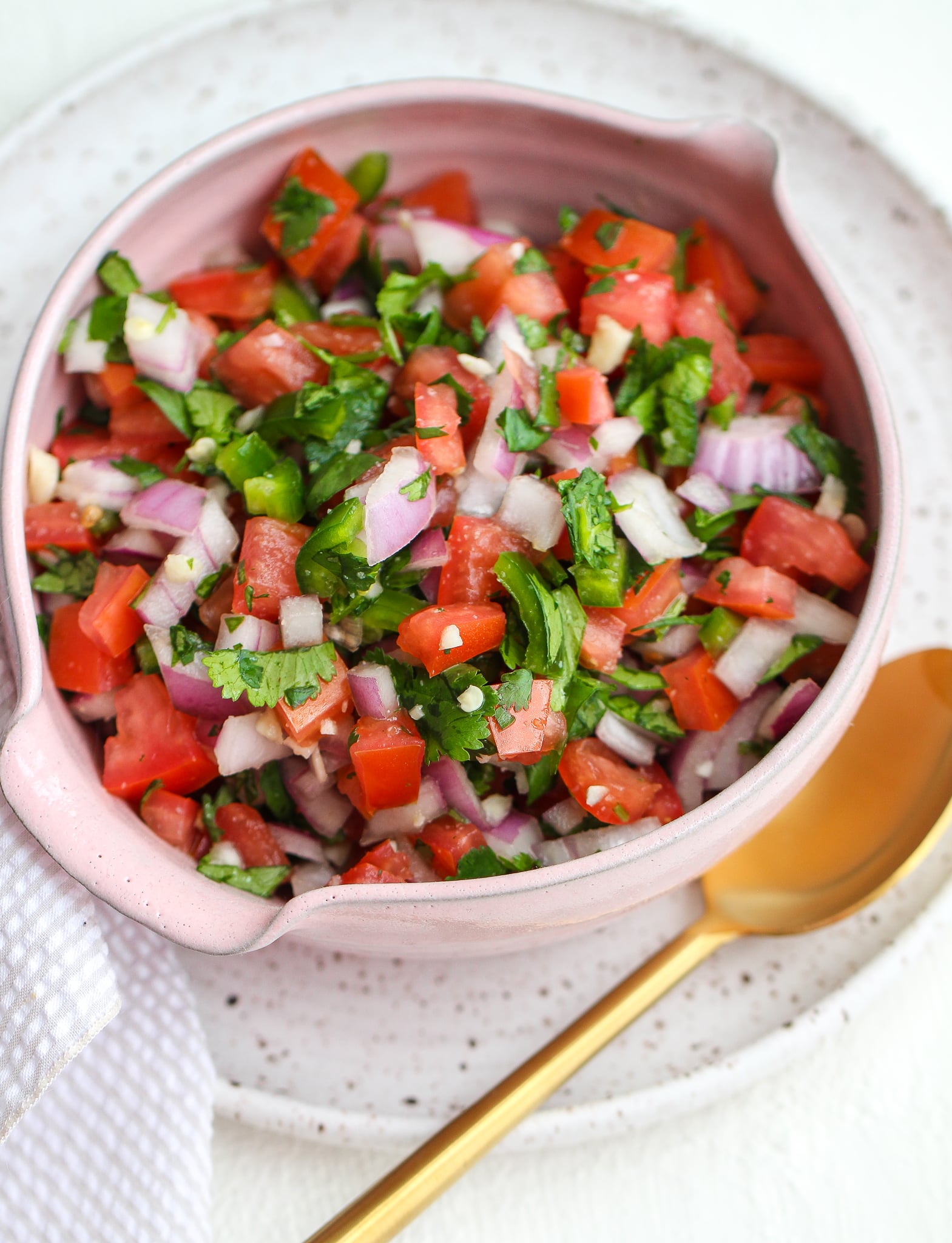 Fresh pico de Gallo (fresh salsa) in a pink bowl with a serving spoon on the side 