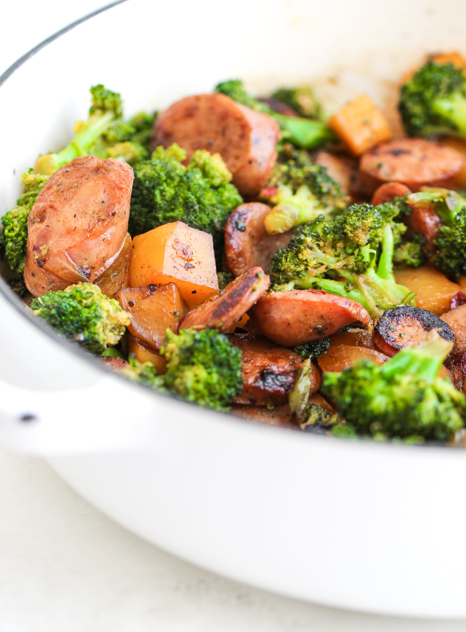 Broccoli, potatoes and chicken sausage in a large white skillet 