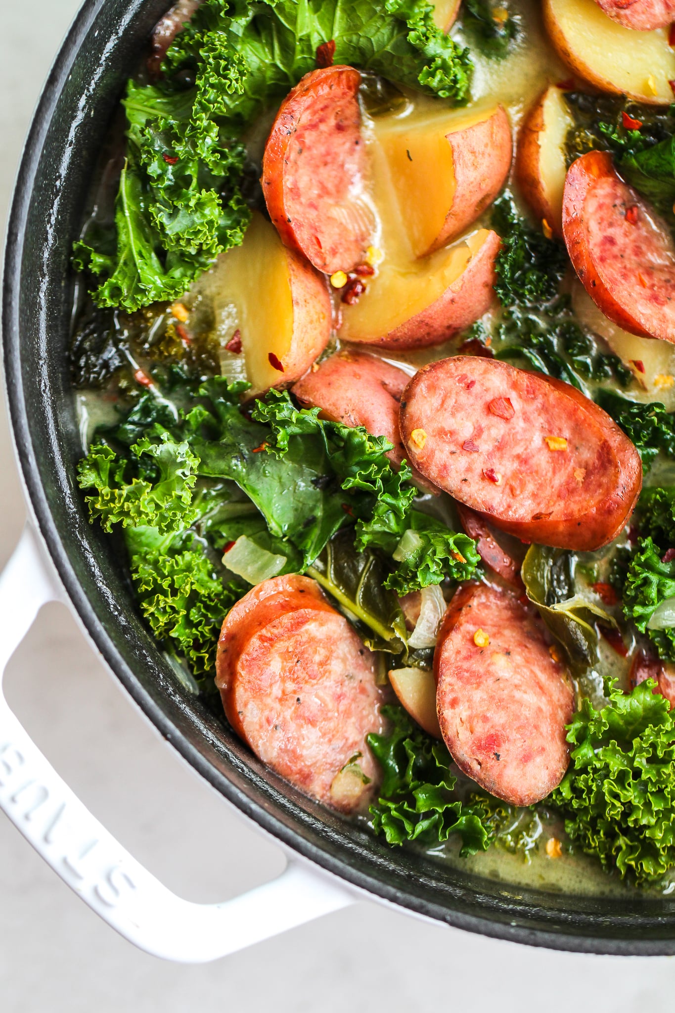 Sausage, kale & potato soup in a white soup pot, topped with pepper flakes