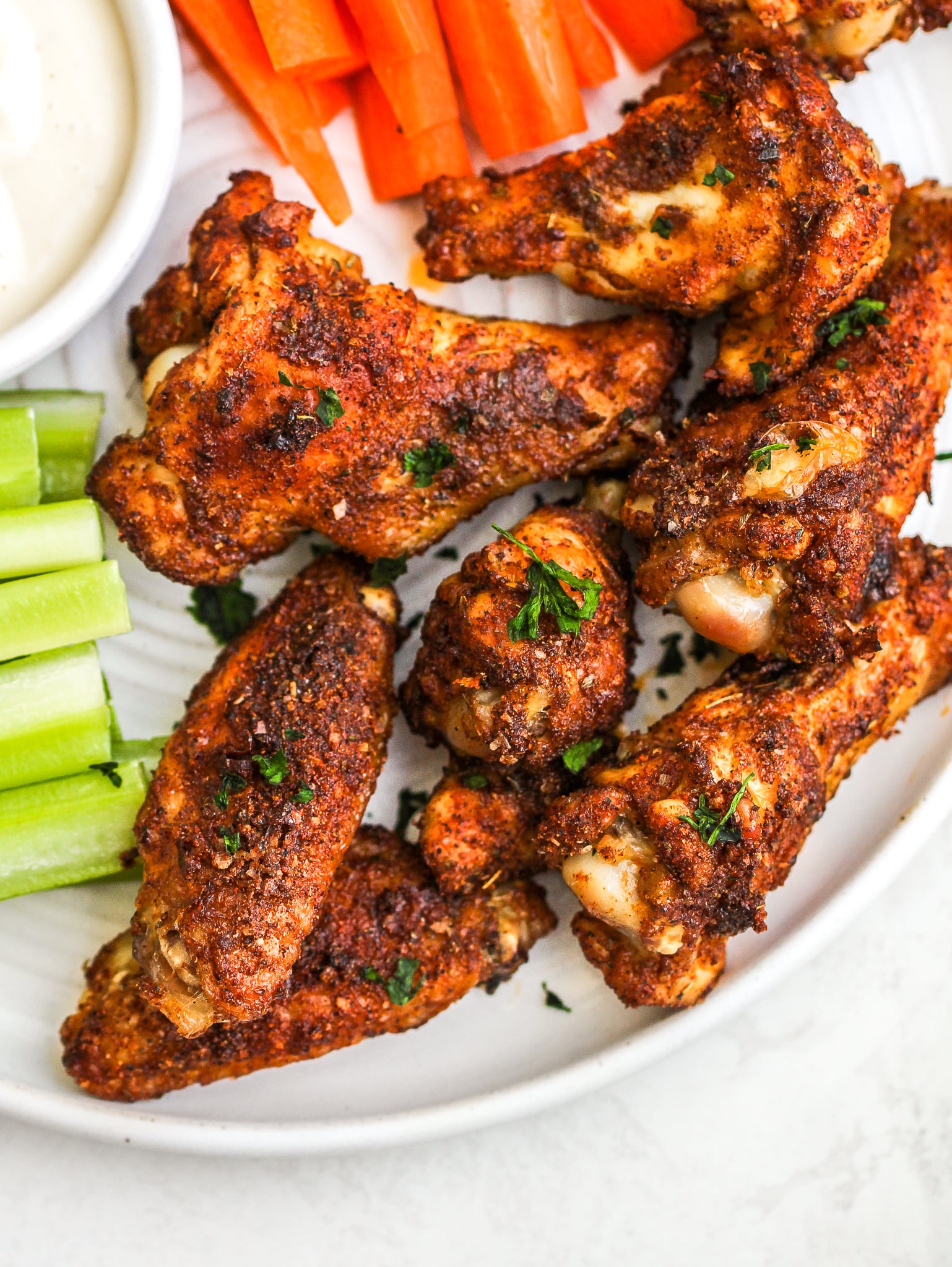 crispy chicken wings seasoned with dry rub on a plate with ranch dressing and carrot and celery sticks 