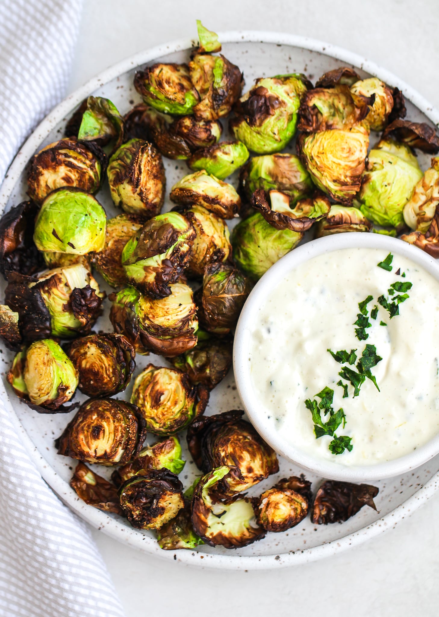 crispy air fryer Brussels sprouts on a ceramic plate with a dipping bowl of lemon garlic aioli 