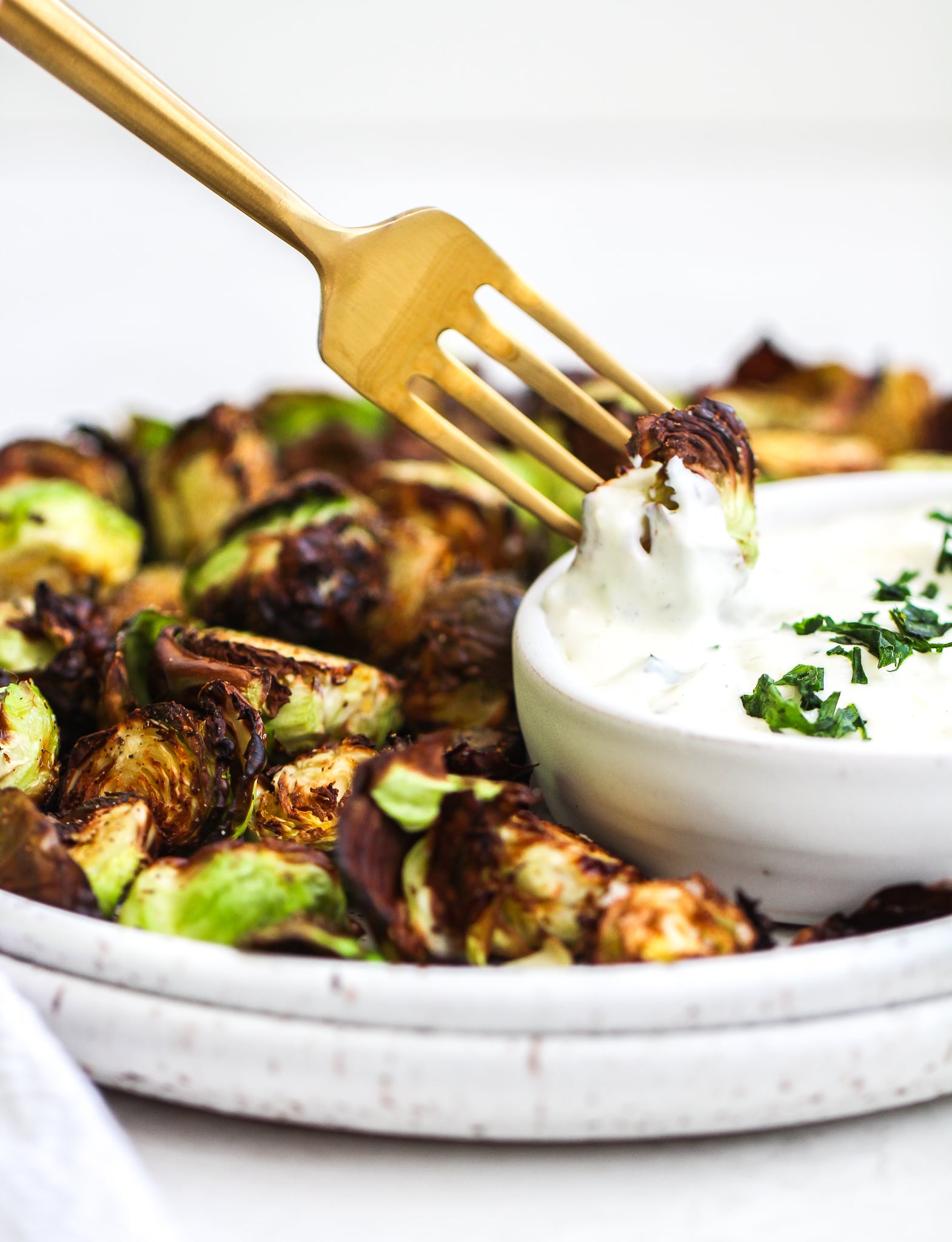matte gold fork dipping a crispy air fryer Brussels sprout in lemon garlic aioli 