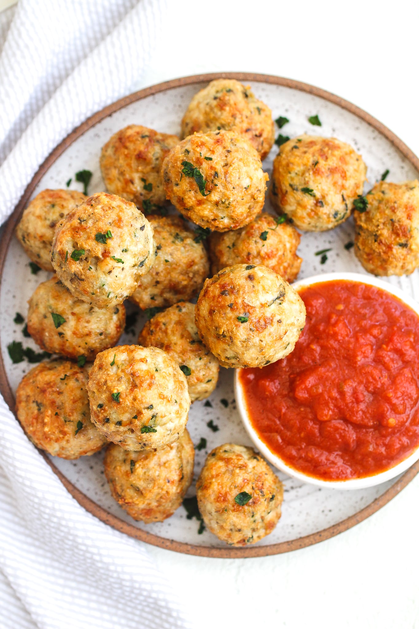 Crispy chicken parmesan meatballs on a ceramic plate topped with fresh parsley and served with a side of marinara sauce 