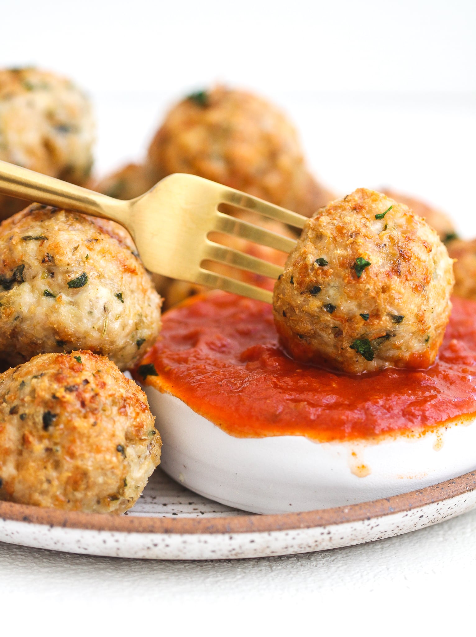 Fork dipping a chicken parmesan meatball into marinara sauce 