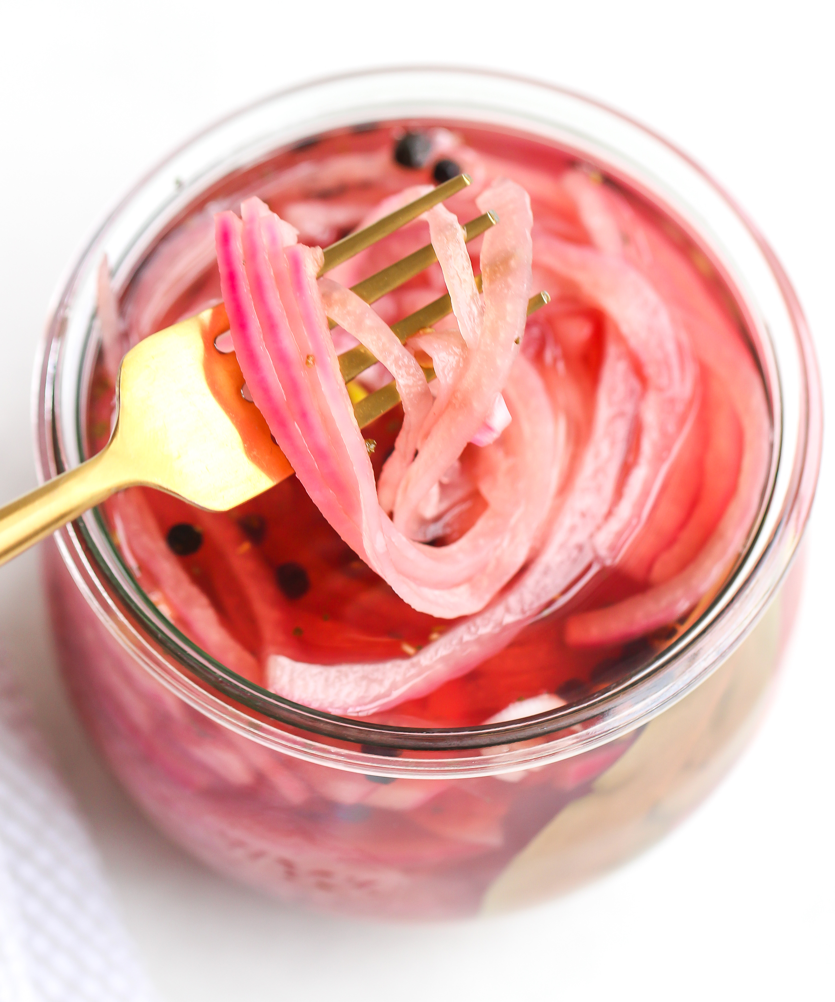 gold fork lifting quick pickled red onions out of a clear glass jar 
