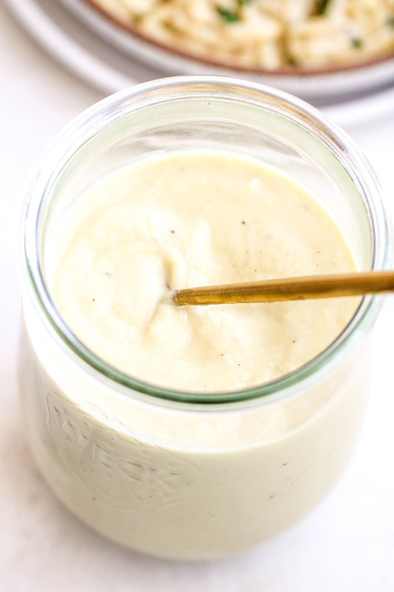creamy roasted garlic alfredo sauce in a glass jar with a gold serving spoon inside it 