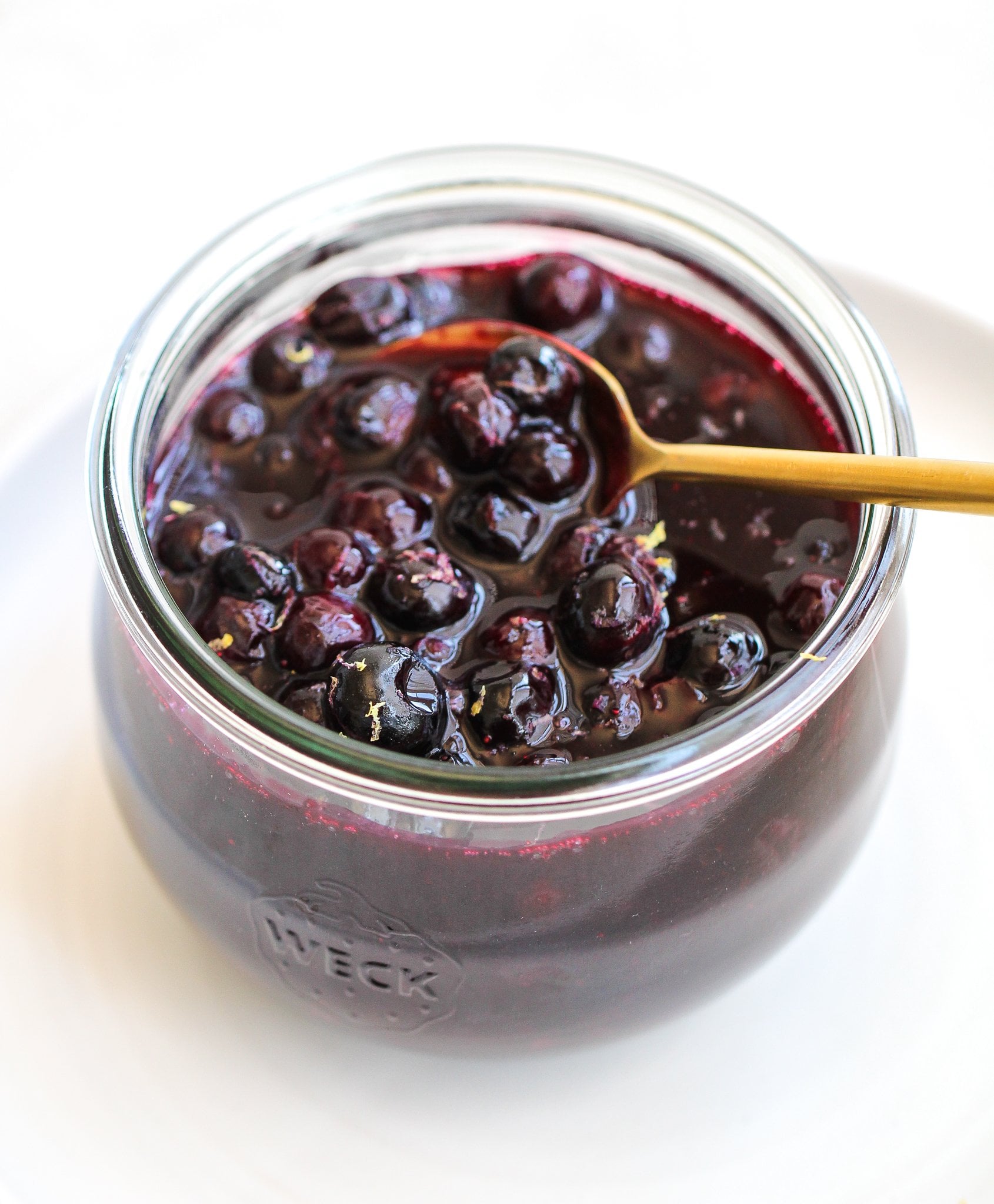 lemon blueberry compote in a glass jar with a gold spoon sitting in it 