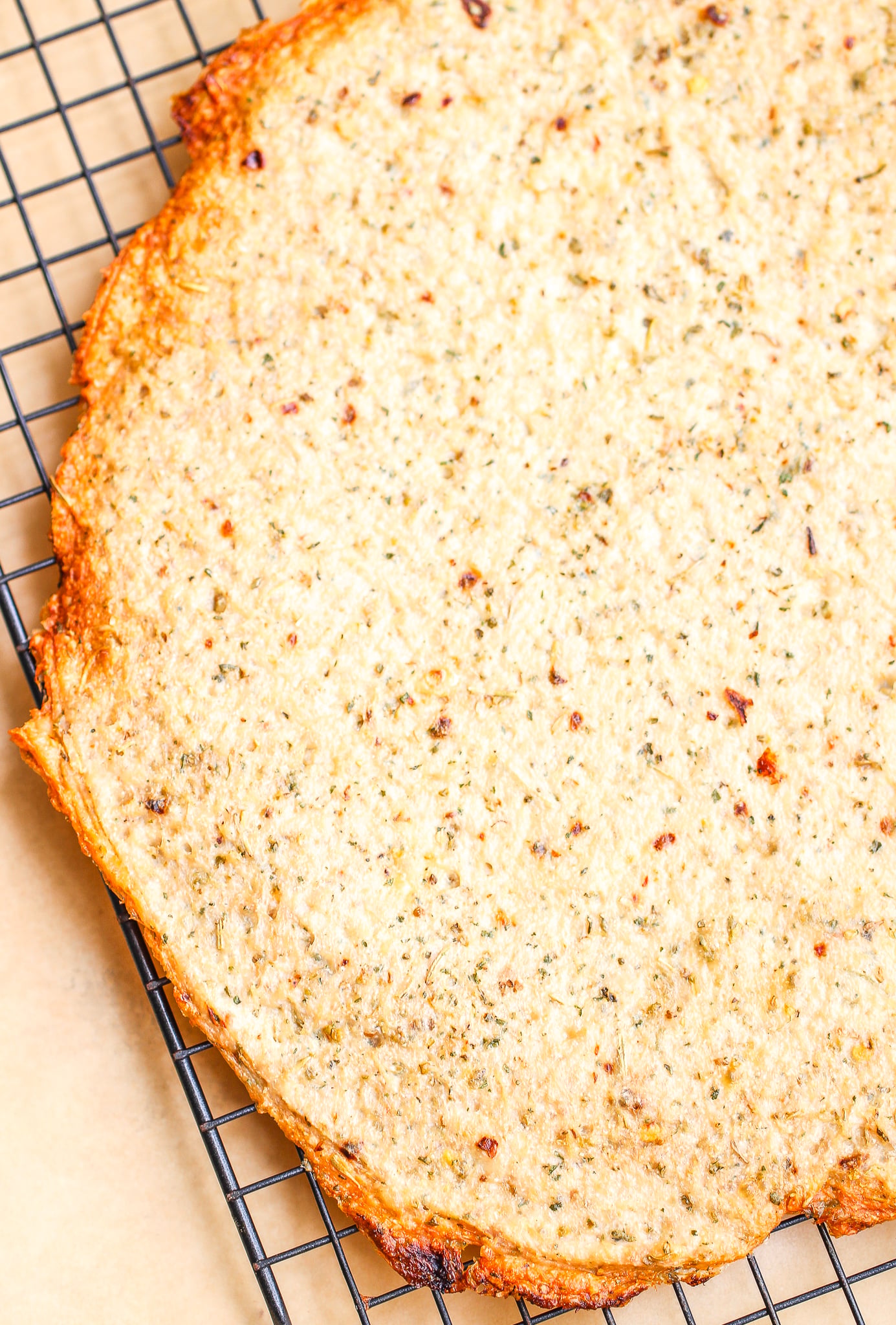 baked low carb ground chicken pizza crust on a baking rack with parchment paper underneath 