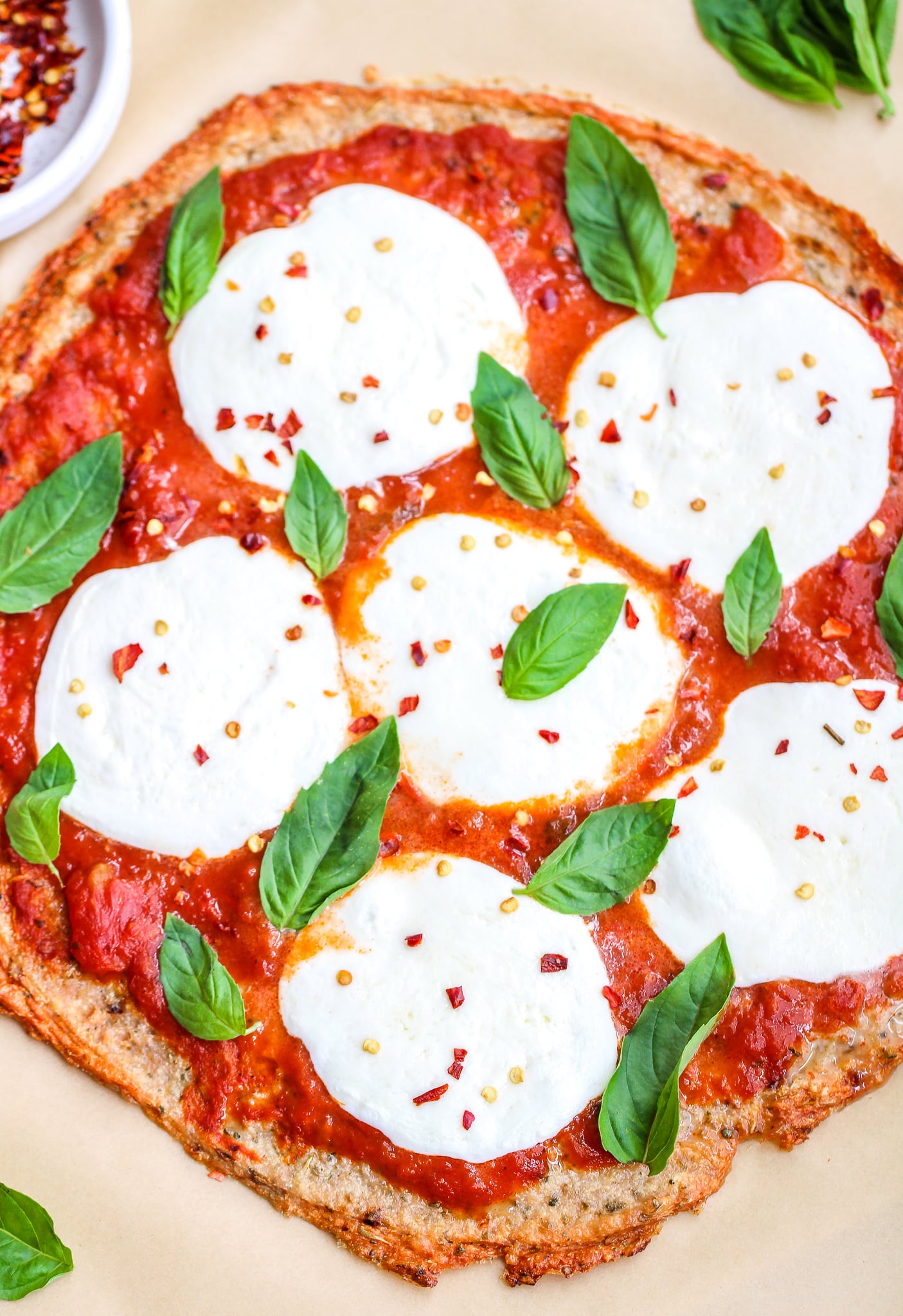 Low carb ground chicken pizza crust topped with marinara sauce, fresh mozzarella and fresh basil leaves. There are red pepper flakes sprinkled on top 