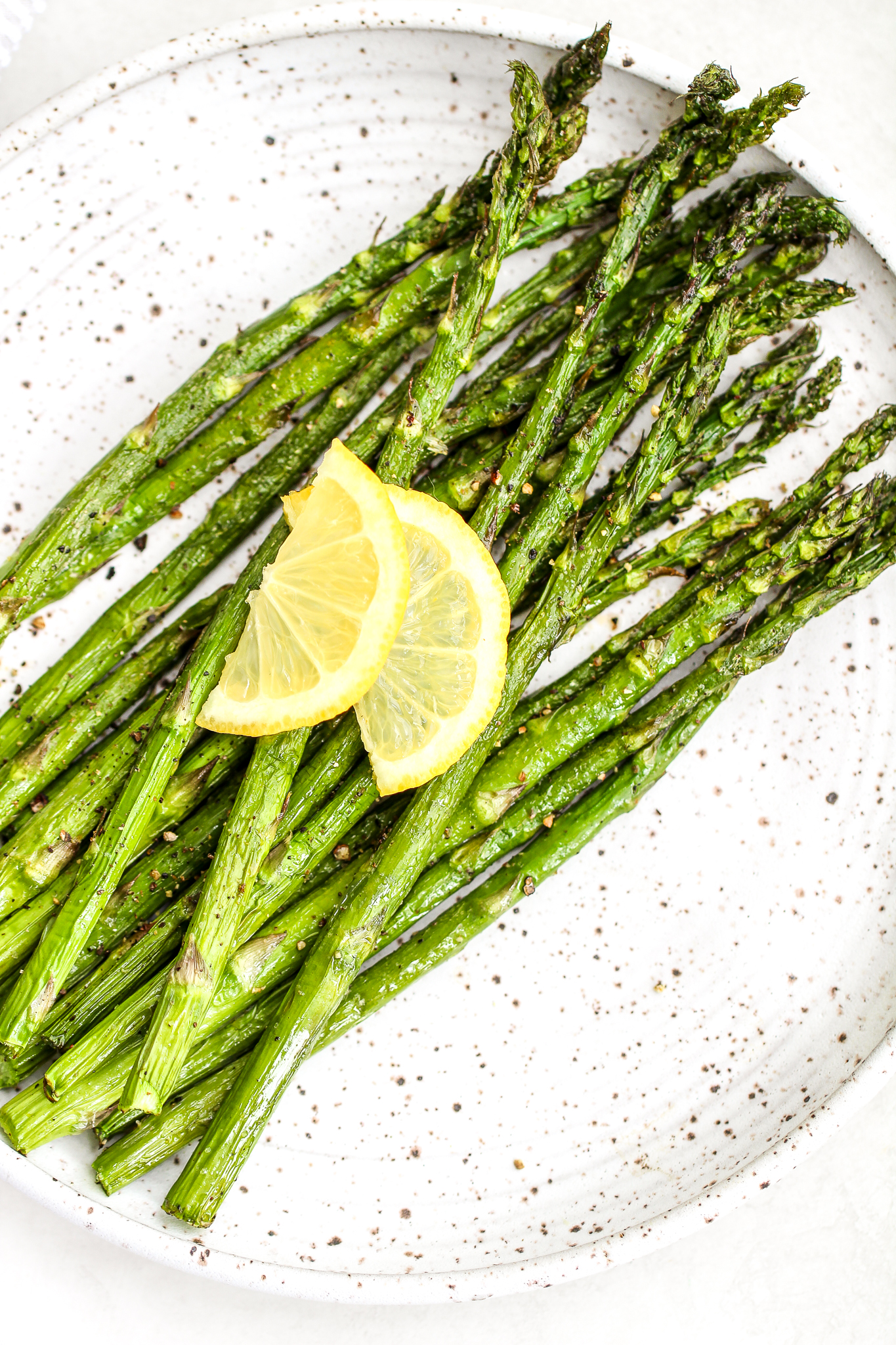 Air fryer asparagus on a ceramic plate topped with fresh cracked pepper and lemon slices 