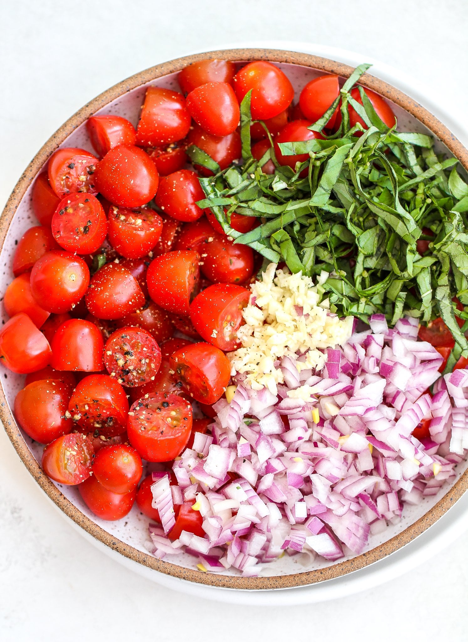 ceramic bowl filled with halved cherry tomatoes, fresh basil, diced red onion and minced garlic 