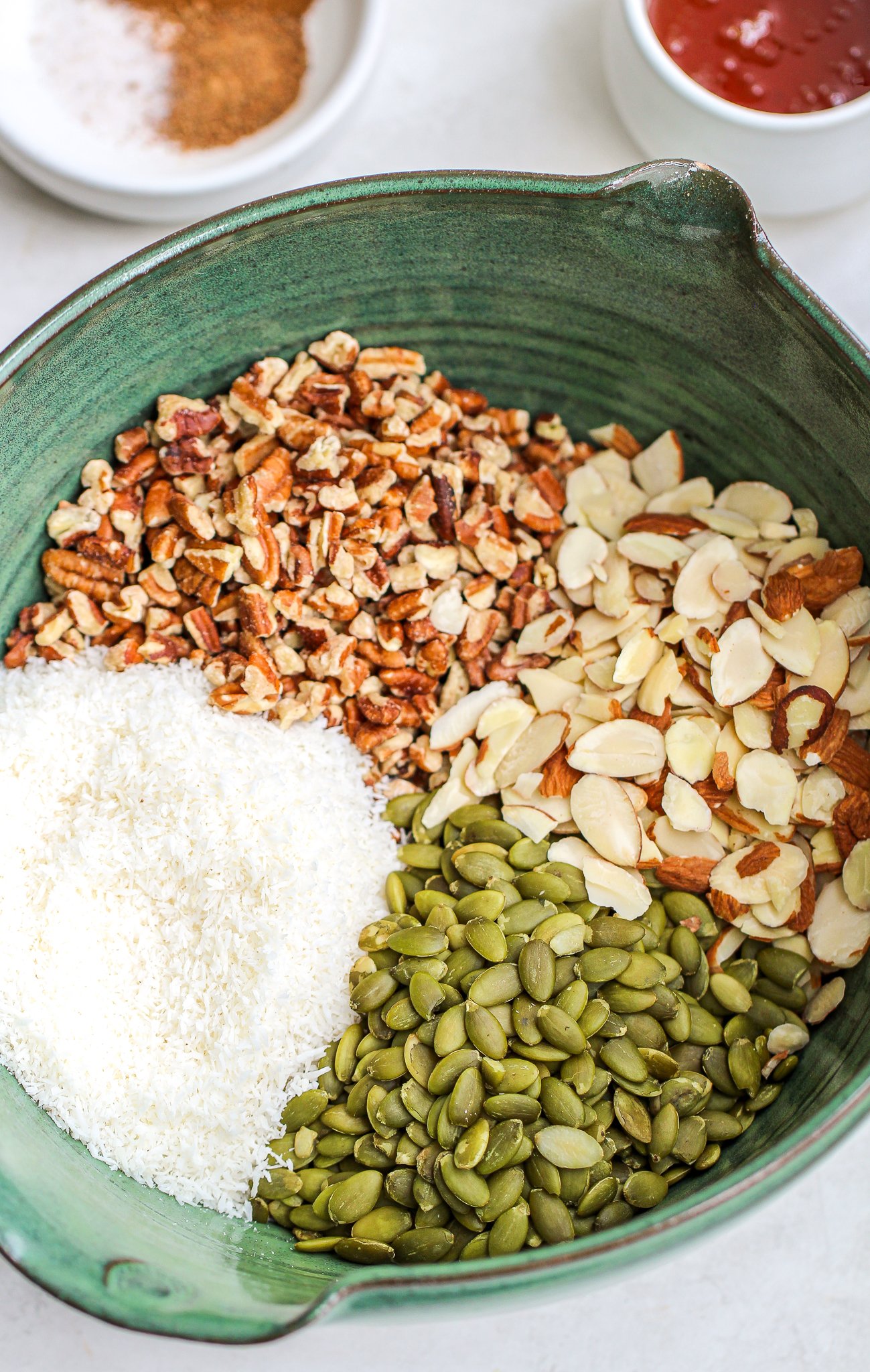 mix of sliced almonds, pecans, shredded coconut, and pumpkin seeds in a large green ceramic mixing bowl
