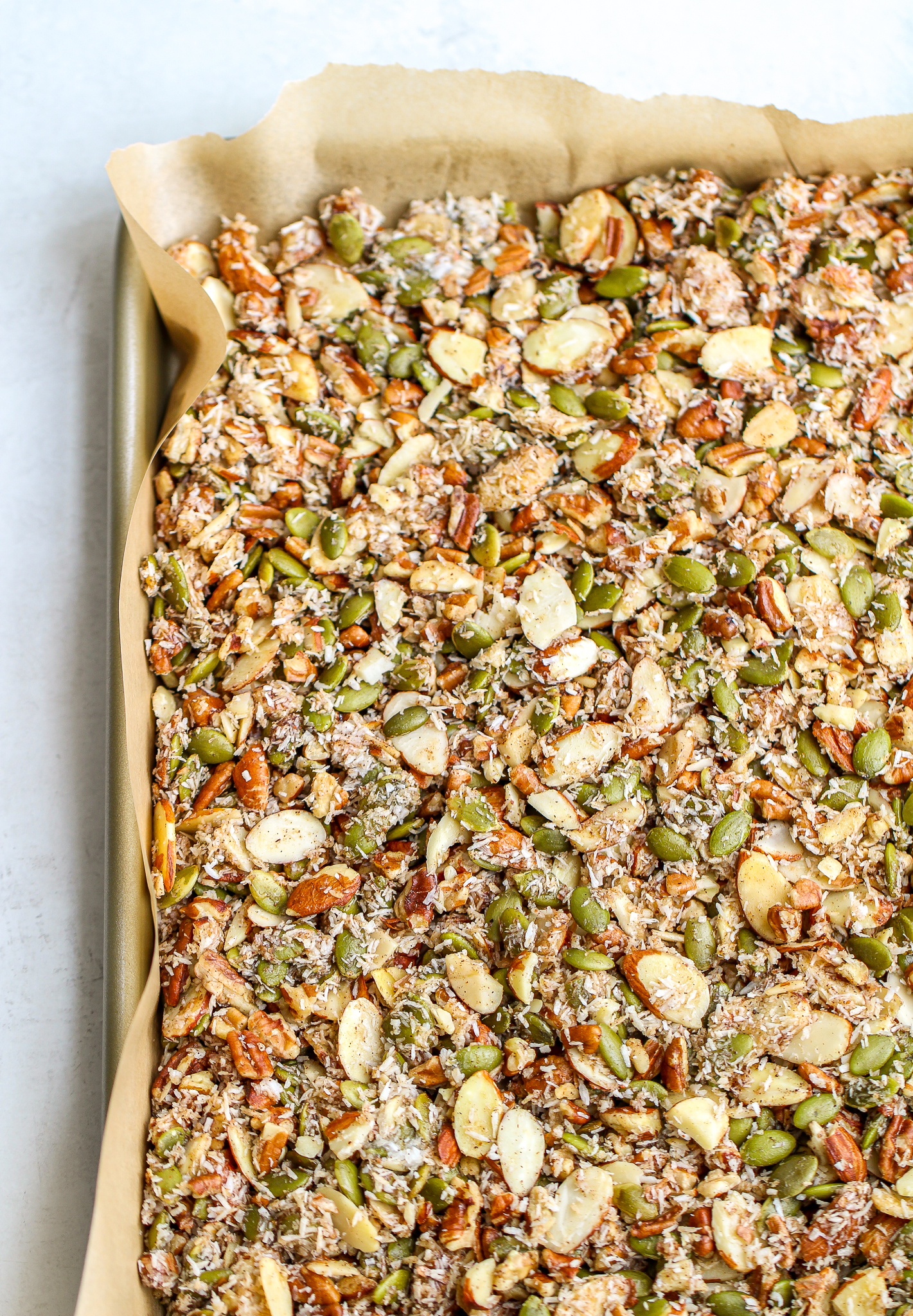 paleo granola spread out on a parchment lined baking sheet before it has been baked 