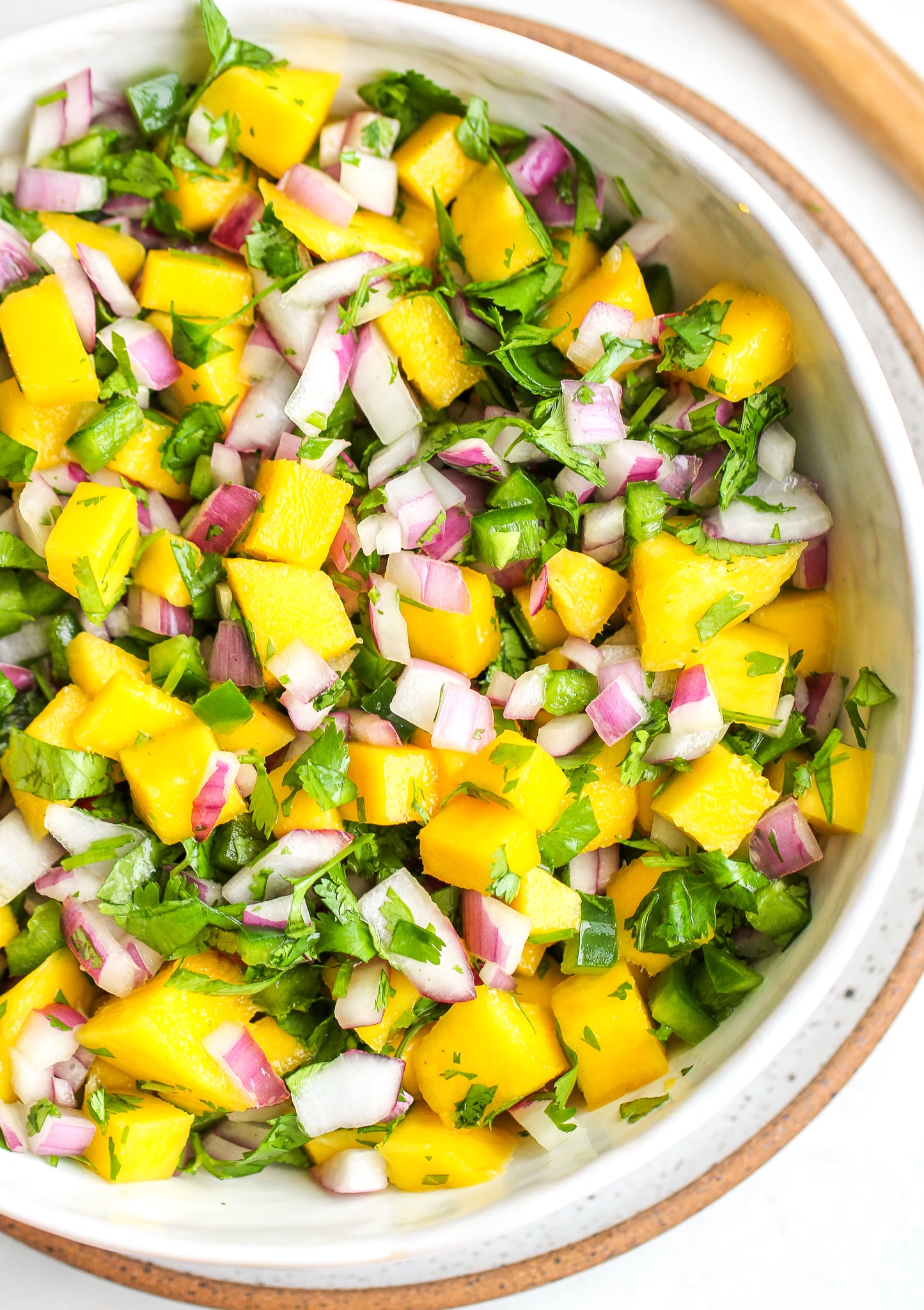 fresh mango salsa in a white serving bowl - there is bright yellow cubed mango, diced green jalapeño, chopped cilantro and diced red onion