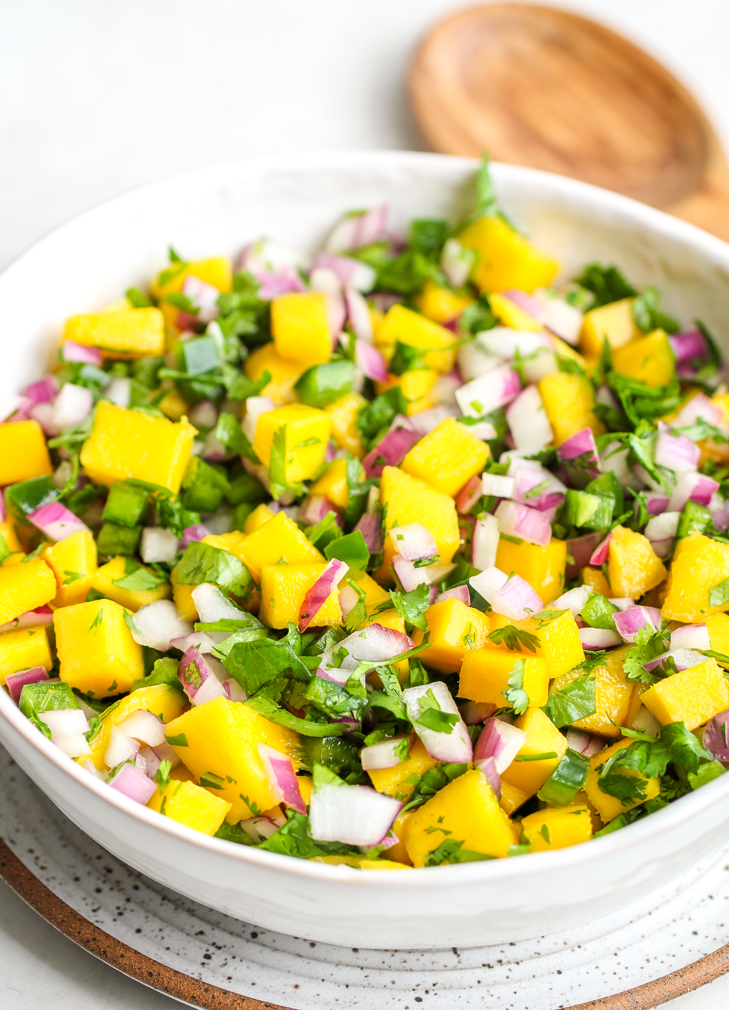 side photo of fresh mango salsa in a white serving bowl - there is bright yellow cubed mango, diced green jalapeño, chopped cilantro and diced red onion